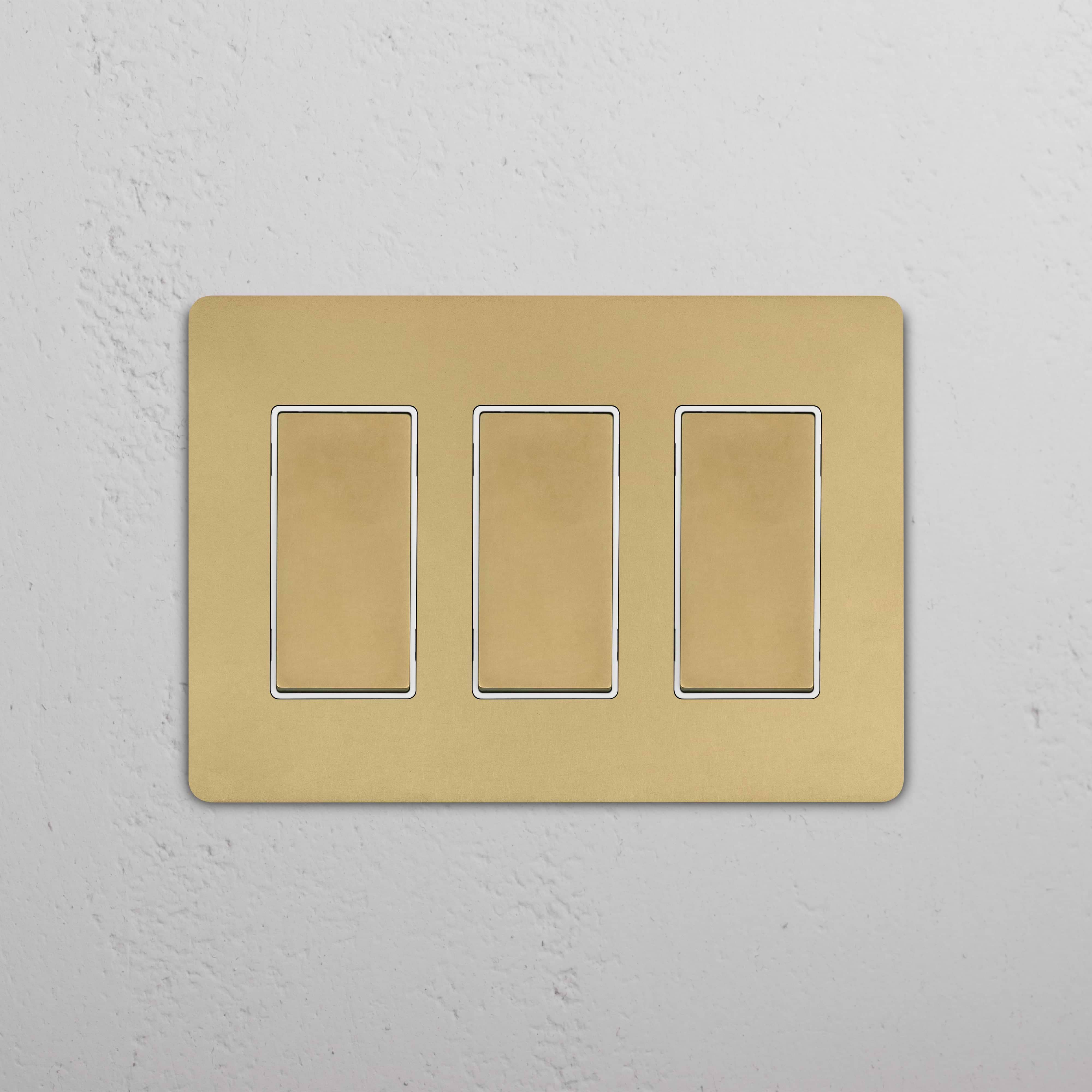Grove 3G Rocker Switch in Antique Brass White with three gold-colored rocker switches on a white plate.