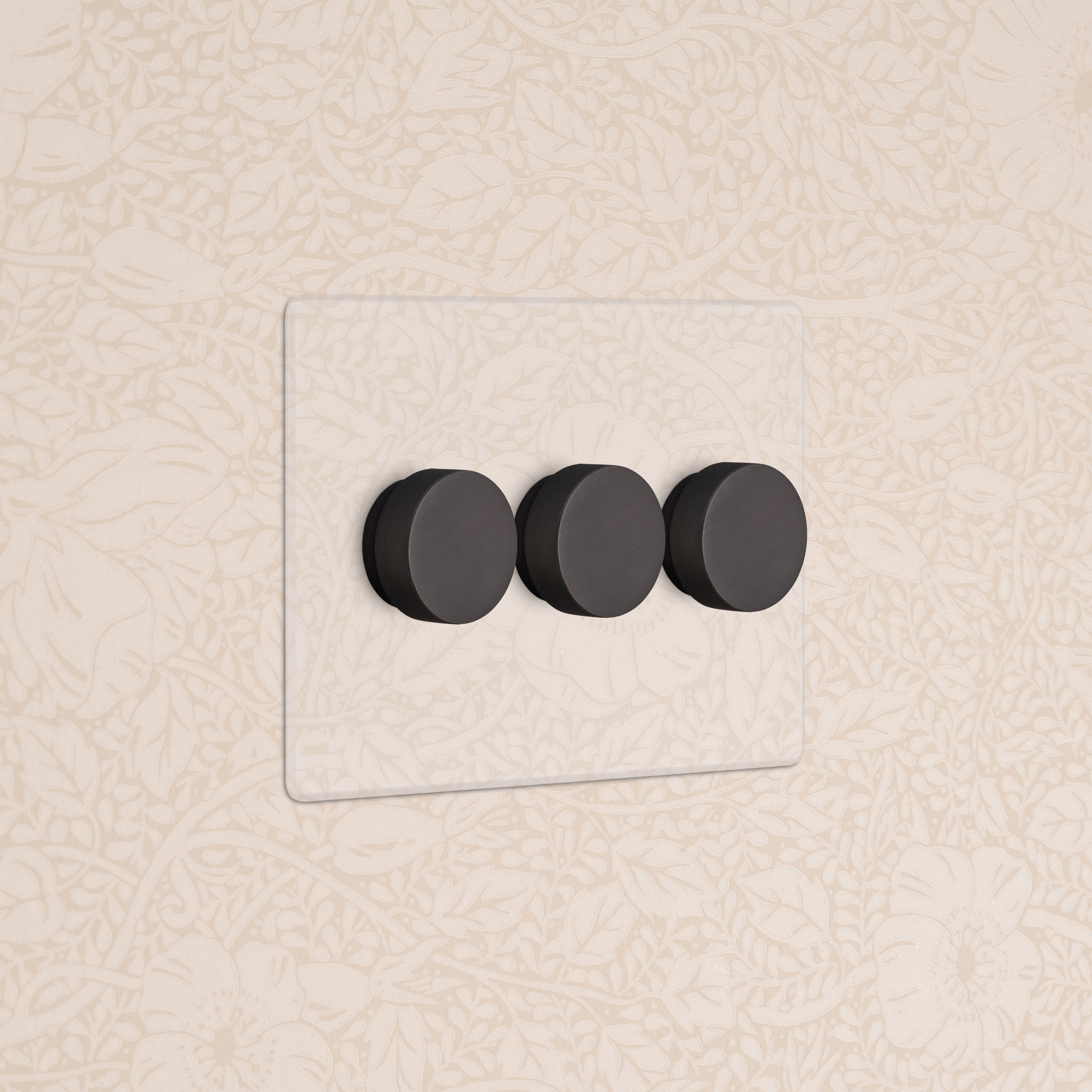 Kew 3G Dimmer Switch in Clear Bronze with three black dials, mounted on a beige floral-patterned wall.