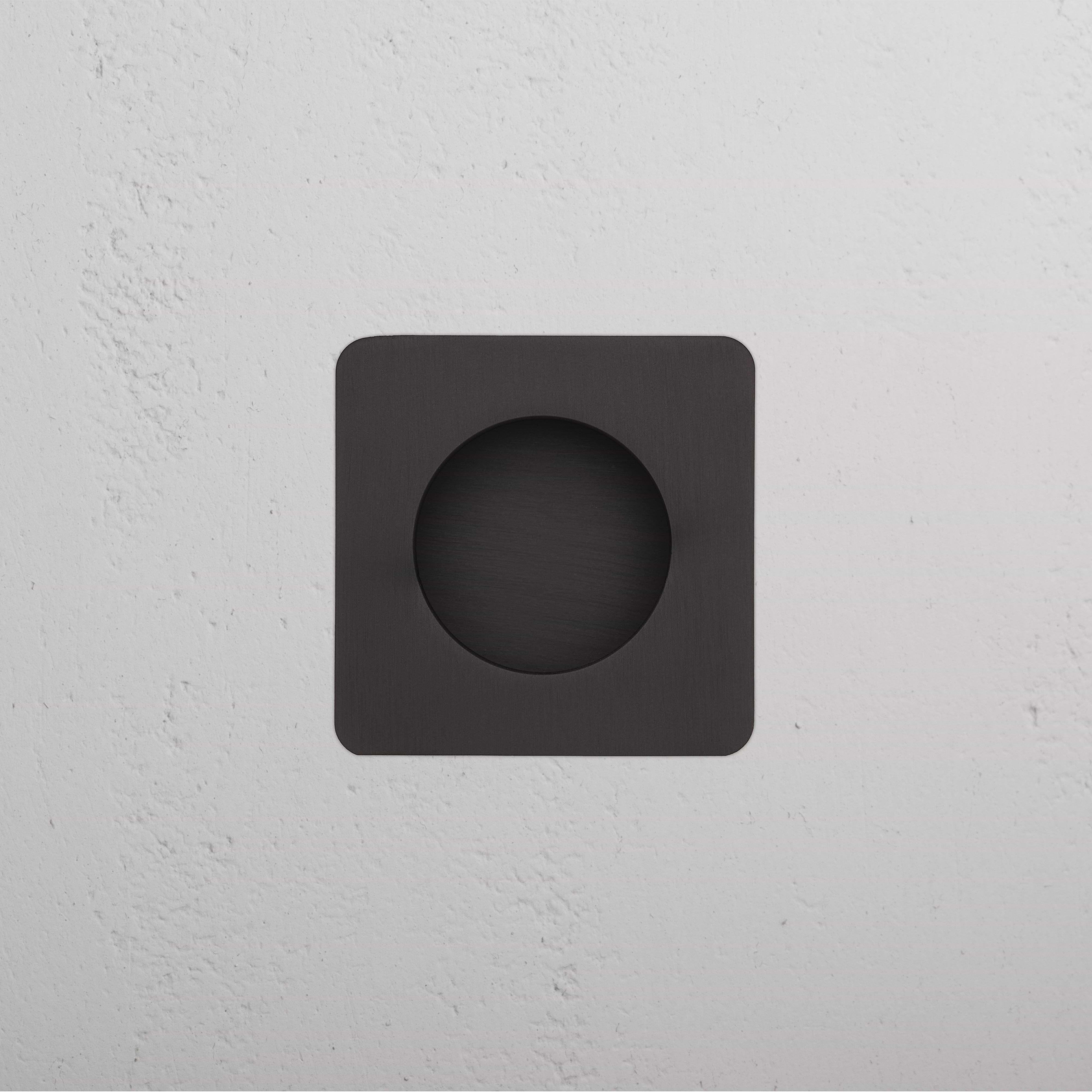 Regent Recessed Small Pull in bronze finish, square shape with circular center, mounted on a white wall.
