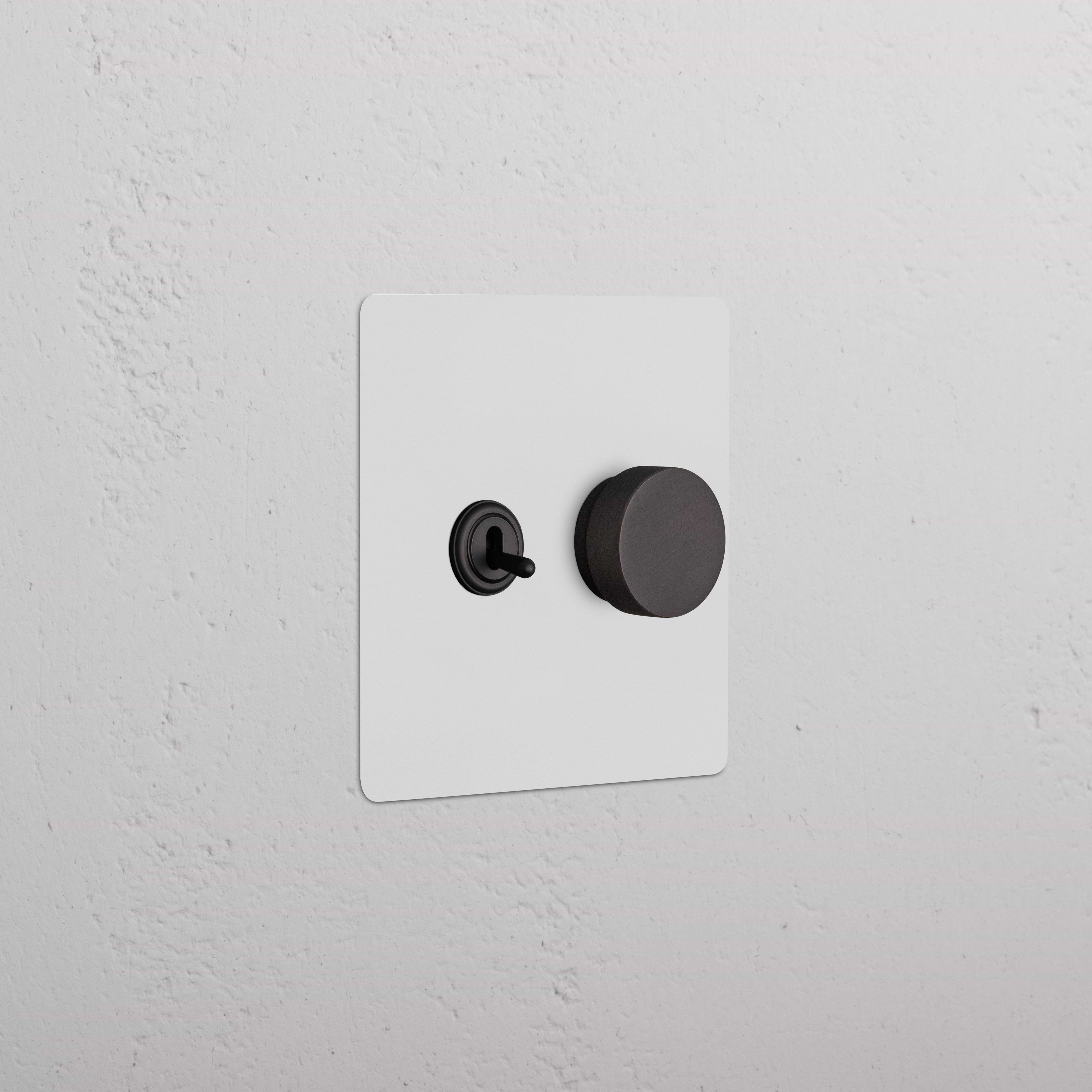 Kew 2G Toggle & Dimmer Switch in paintable bronze, with black toggle and round dimmer knob on white wall.