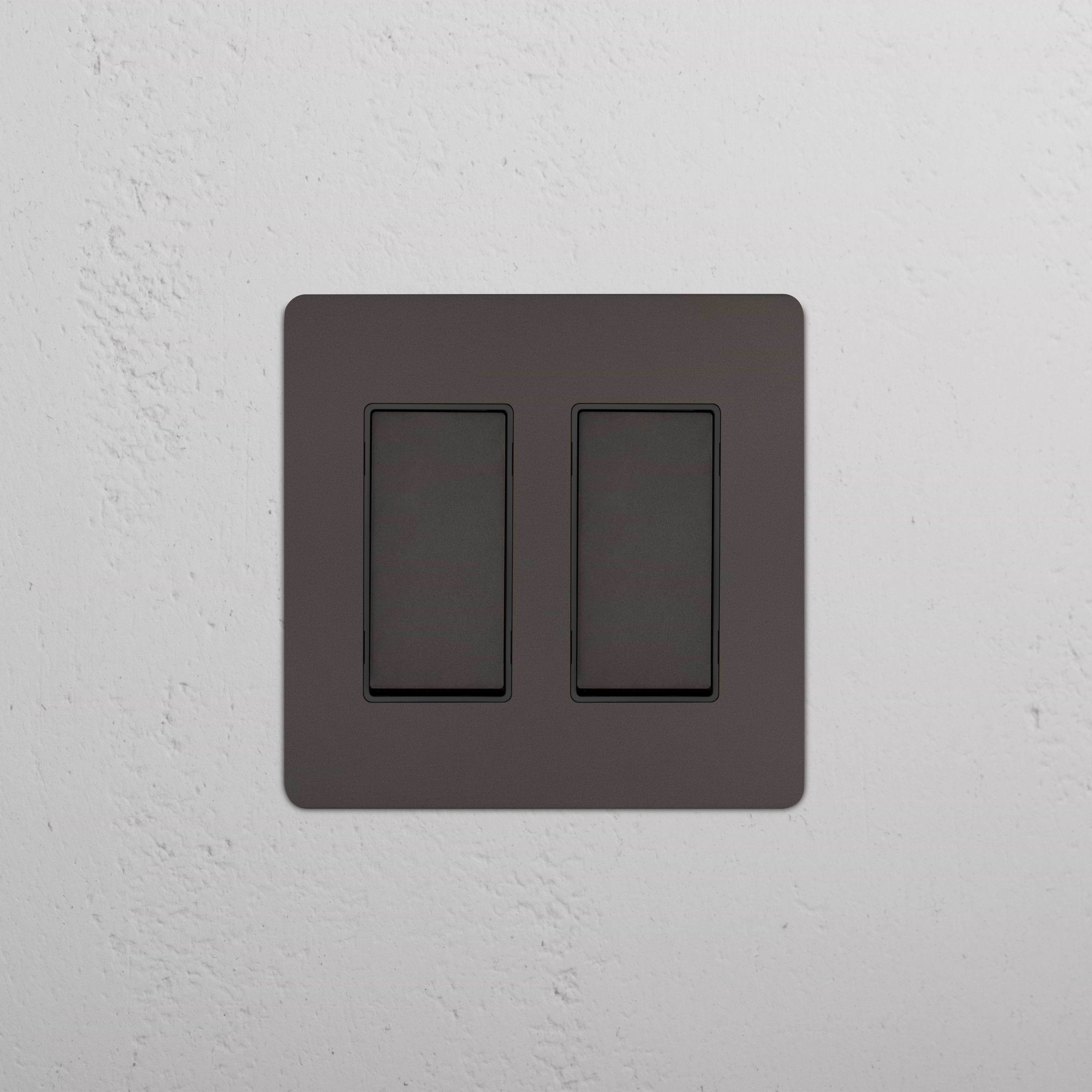 Kew 2G Rocker Switch in Bronze Black, mounted on a white textured wall.