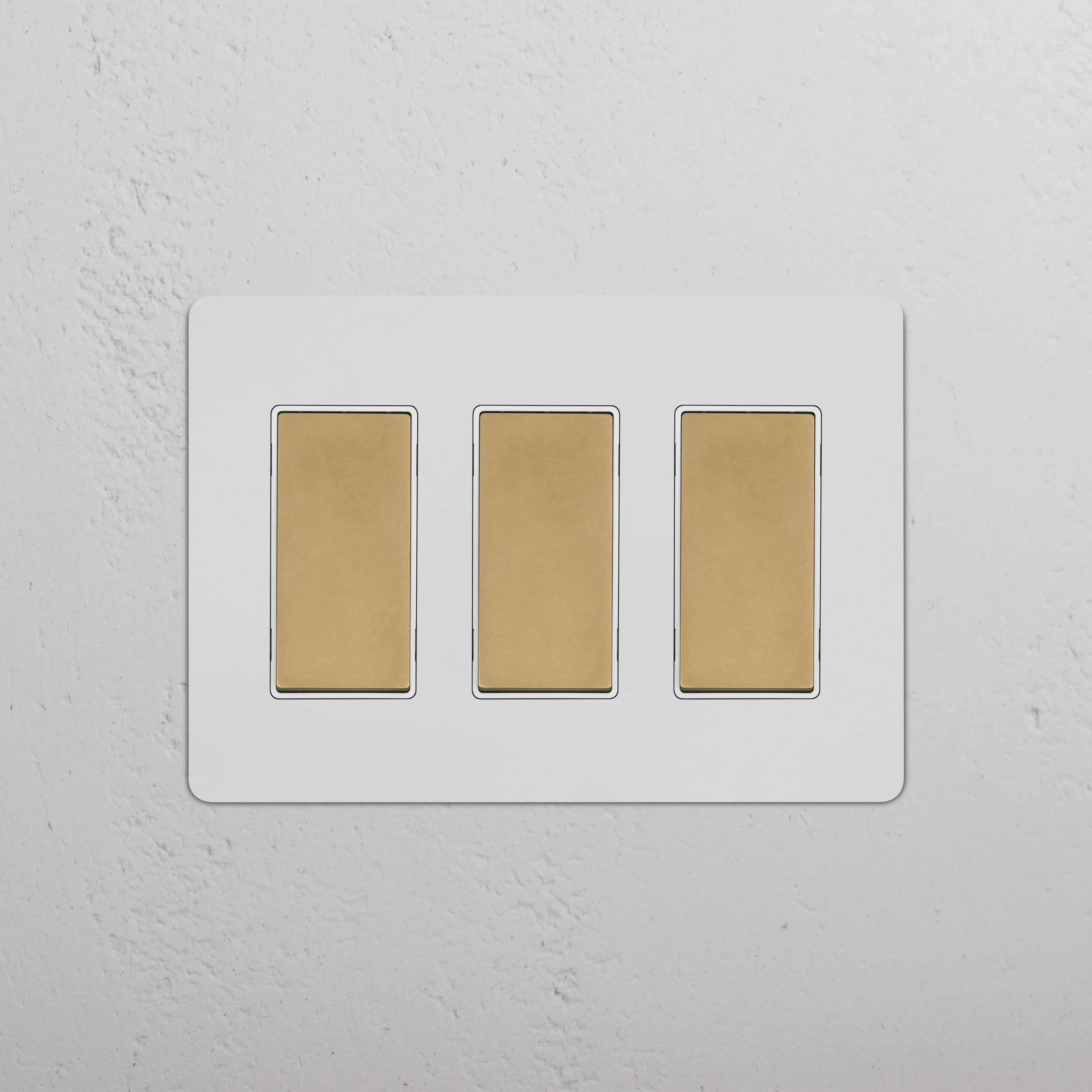 Kew 3G Rocker Switch in Paintable Antique Brass White with three gold rocker switches on a white plate.