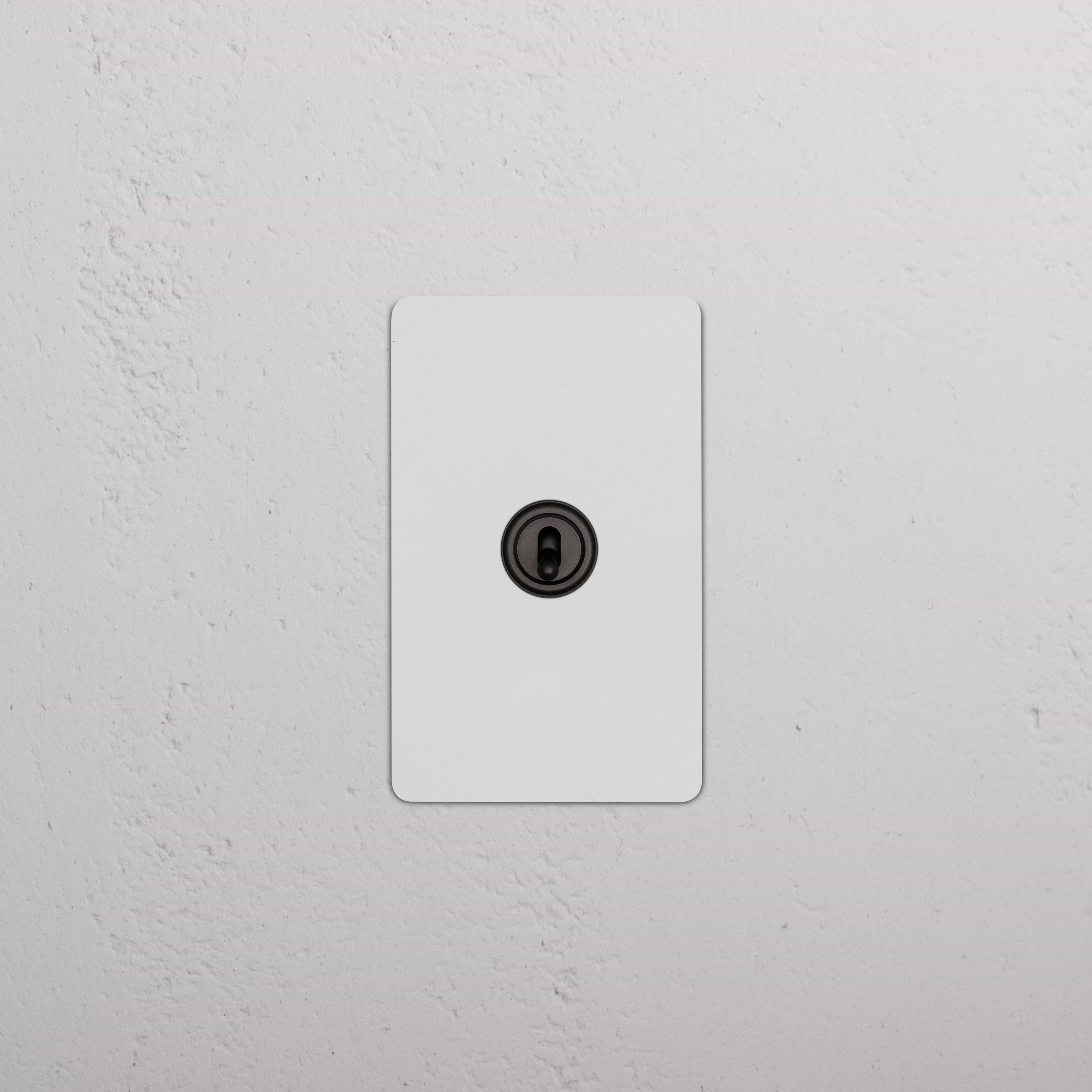 Kew 1G Dimming Retractive Toggle Switch in paintable bronze finish, mounted on a wall.
