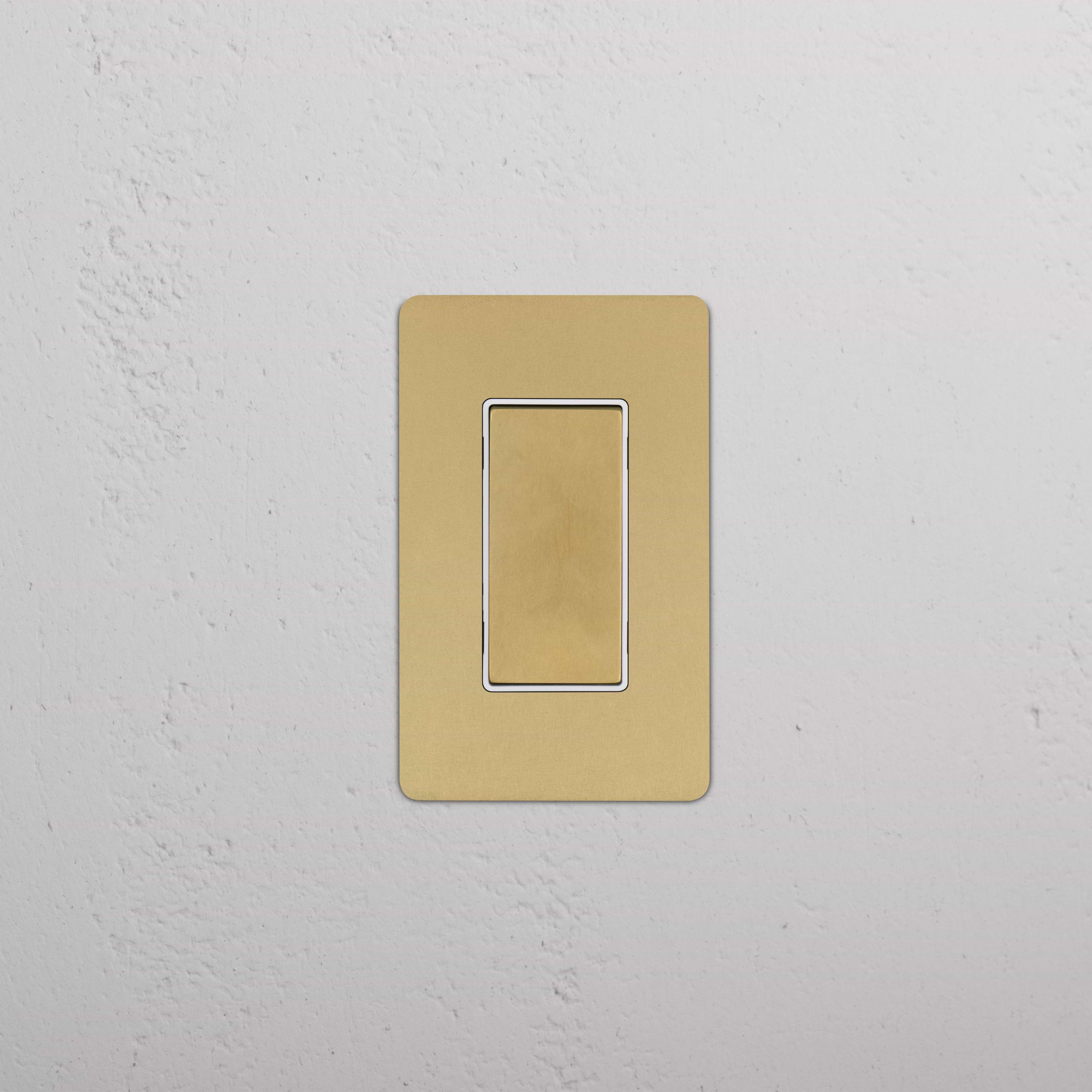 Kew 1G Center Retractive Rocker Switch in antique brass white finish, mounted on a white wall.