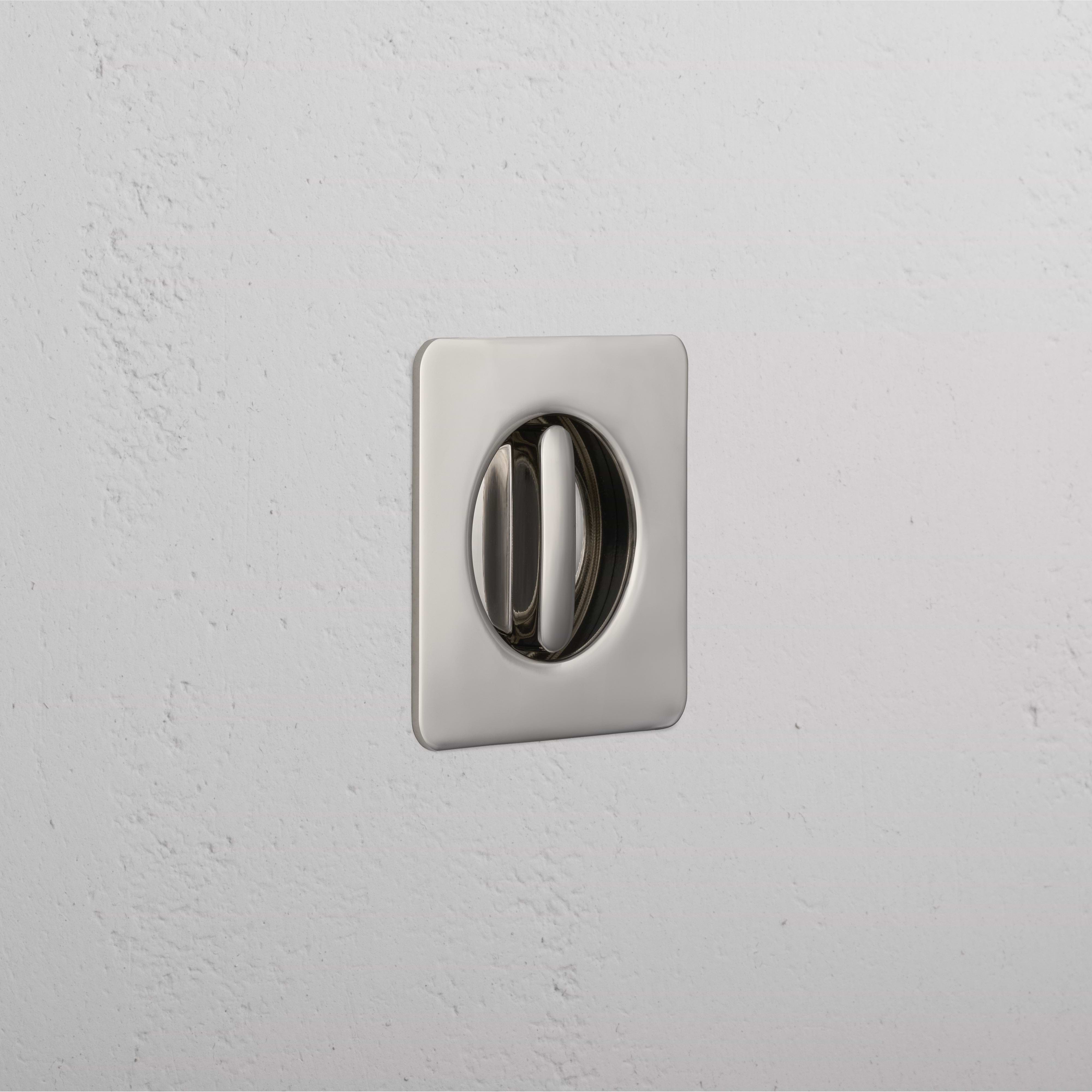 Polished nickel Regent Recessed Thumbturn with square plate, mounted on a white textured wall.