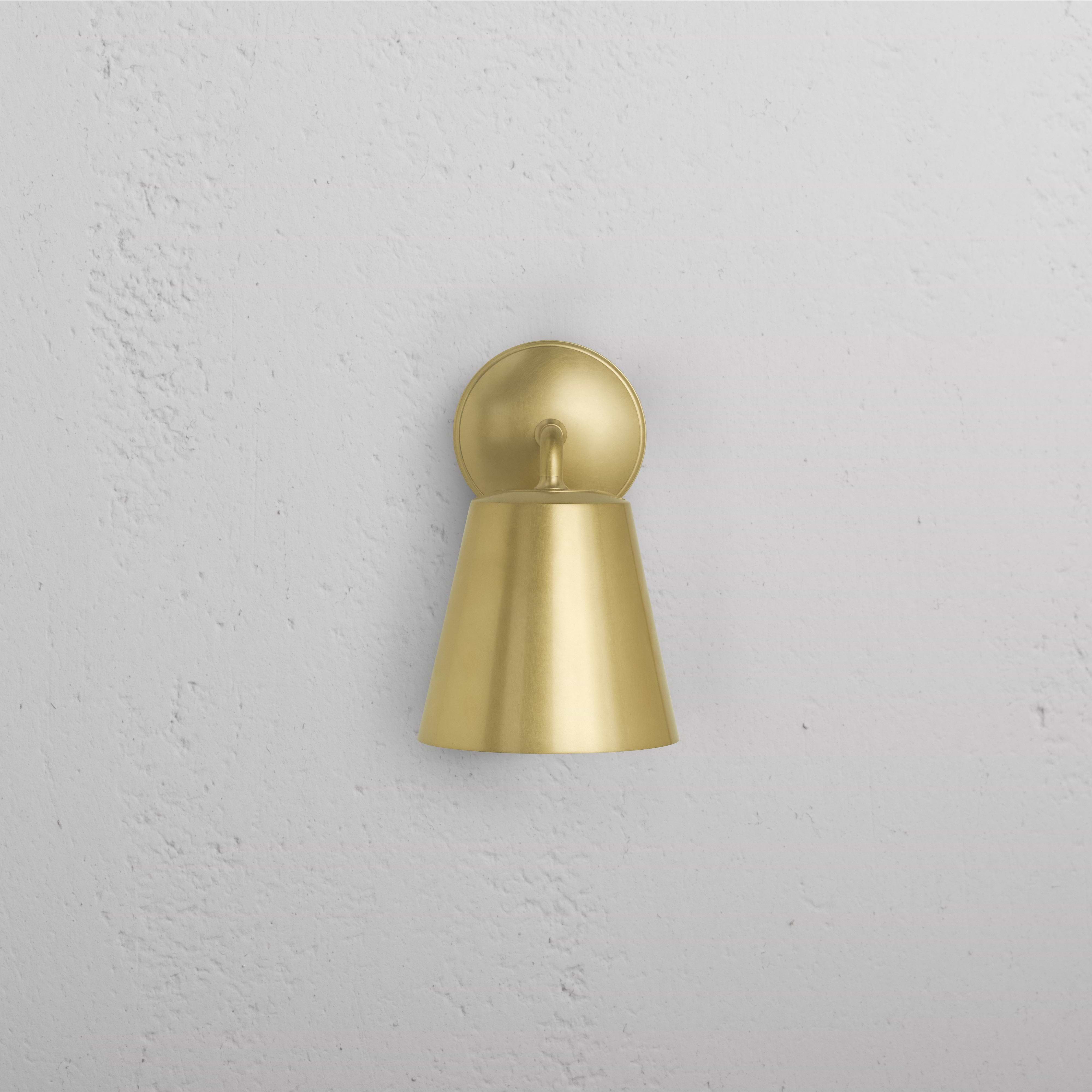 Richmond Medium Wall Light in antique brass with cone-shaped shade and round base, mounted on a white wall.