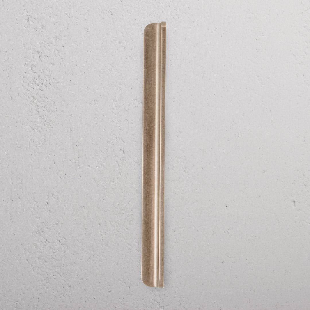 Medium-sized Oxford Furniture Handle in antique brass finish, mounted vertically on a white textured surface.