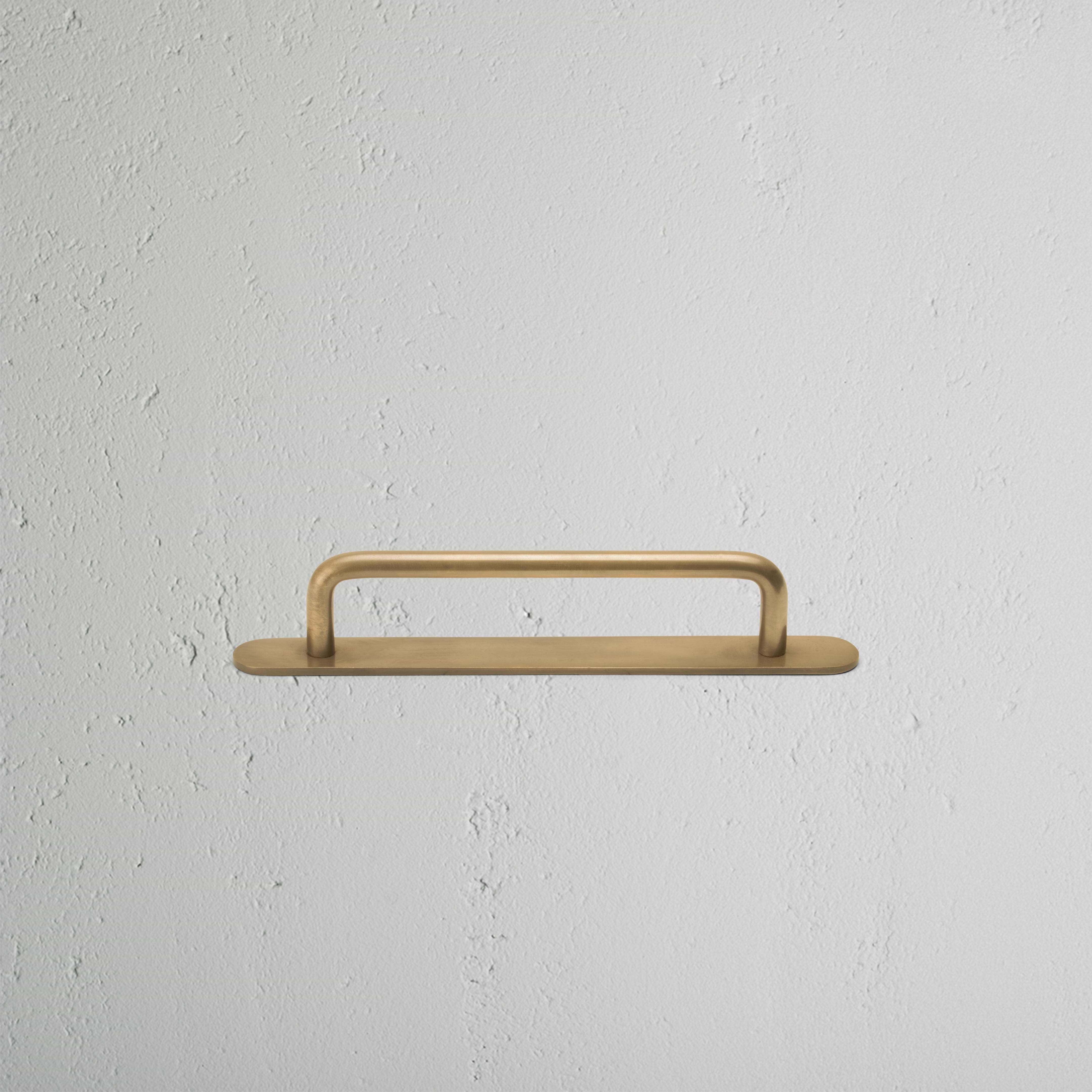 Kilburn Furniture Handle Small in antique brass, mounted horizontally on a textured white wall.