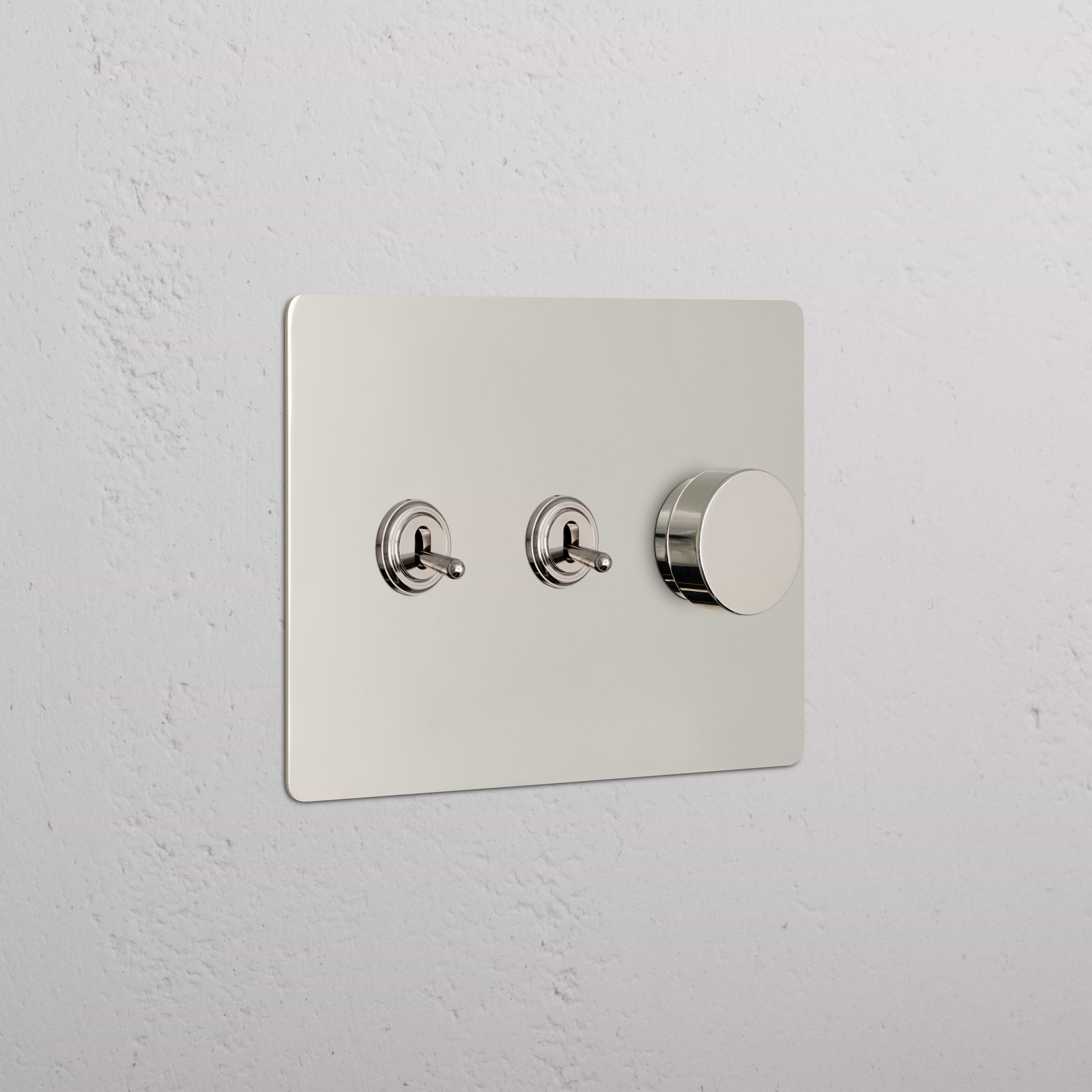 Polished nickel Kew 3G 2x Toggle & Dimmer Switch with two toggle switches and one dimmer knob on wall.