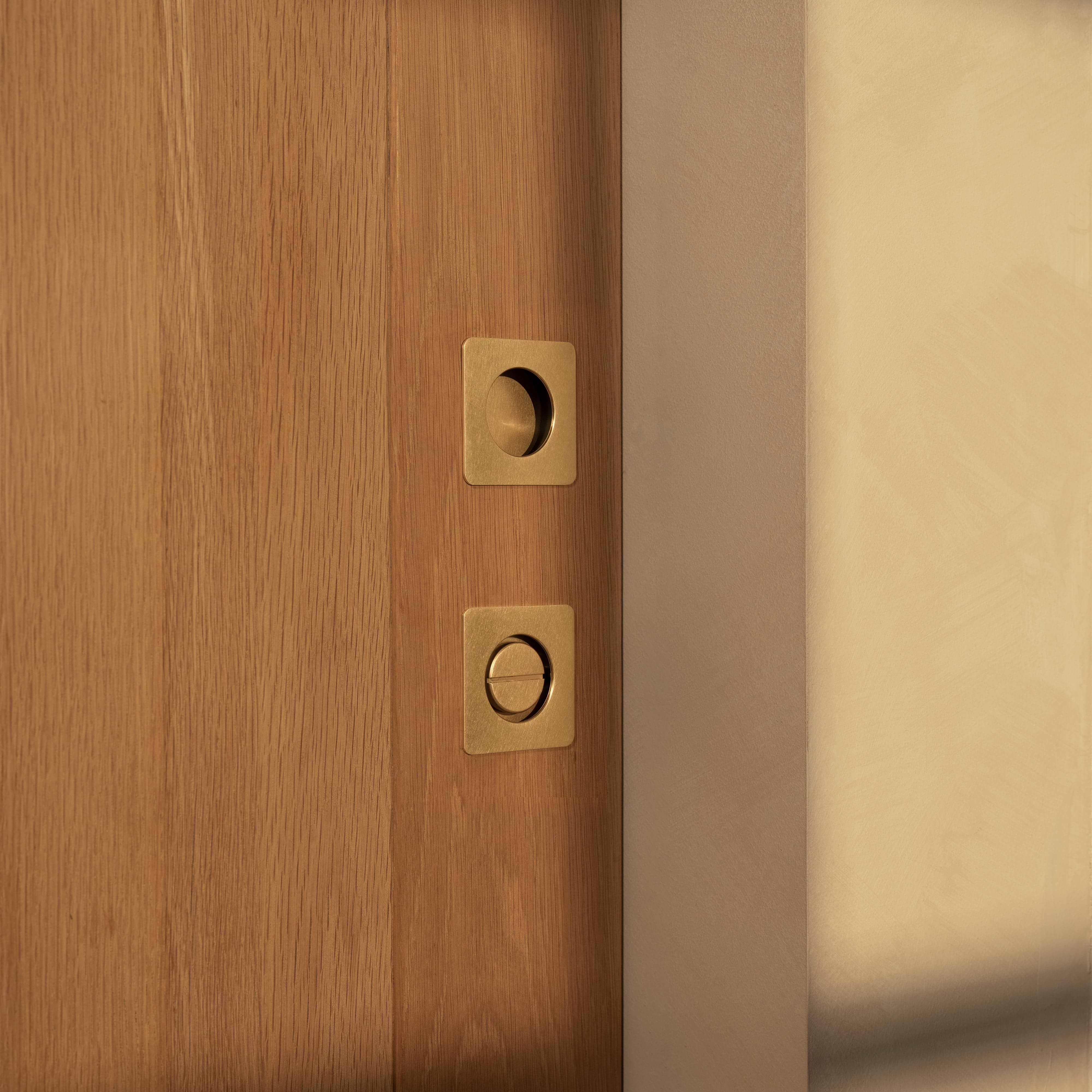 Regent Recessed Small Pull in antique brass, shown installed vertically on a wooden door.