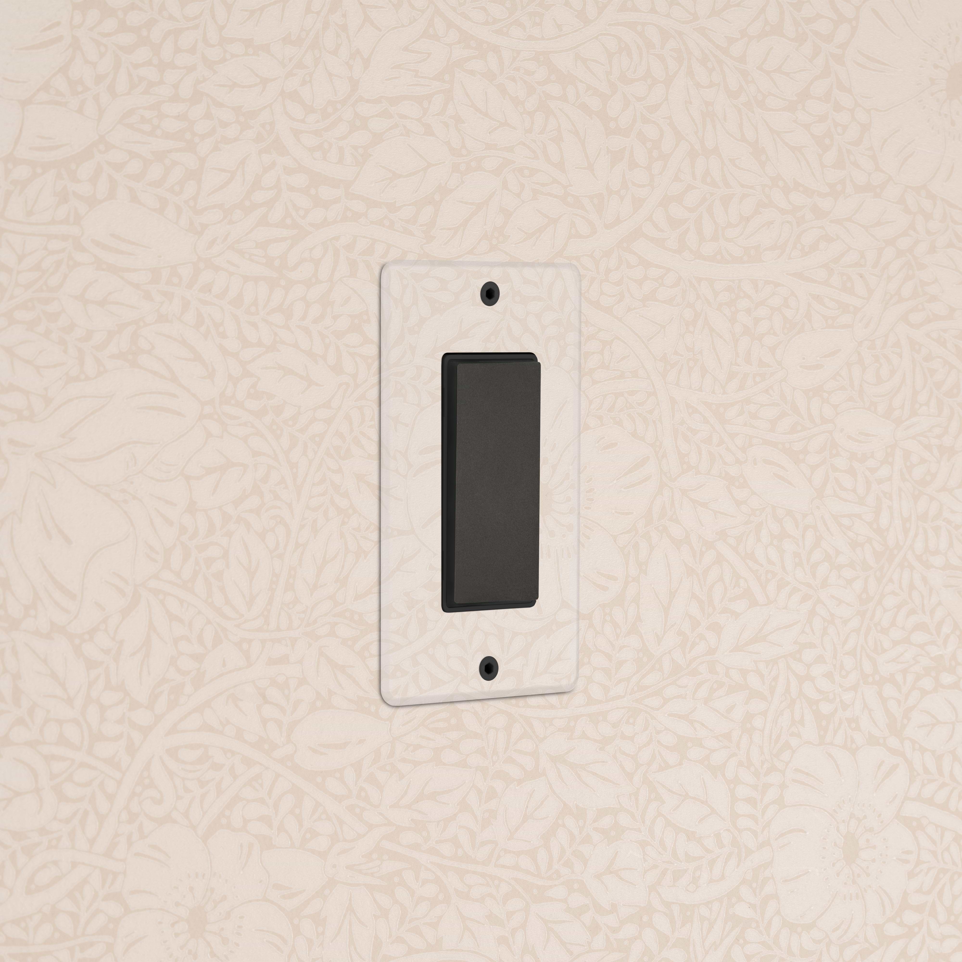 Kew 1G Center Retractive Rocker Switch in Clear Bronze Black, mounted on a floral-patterned beige wall.