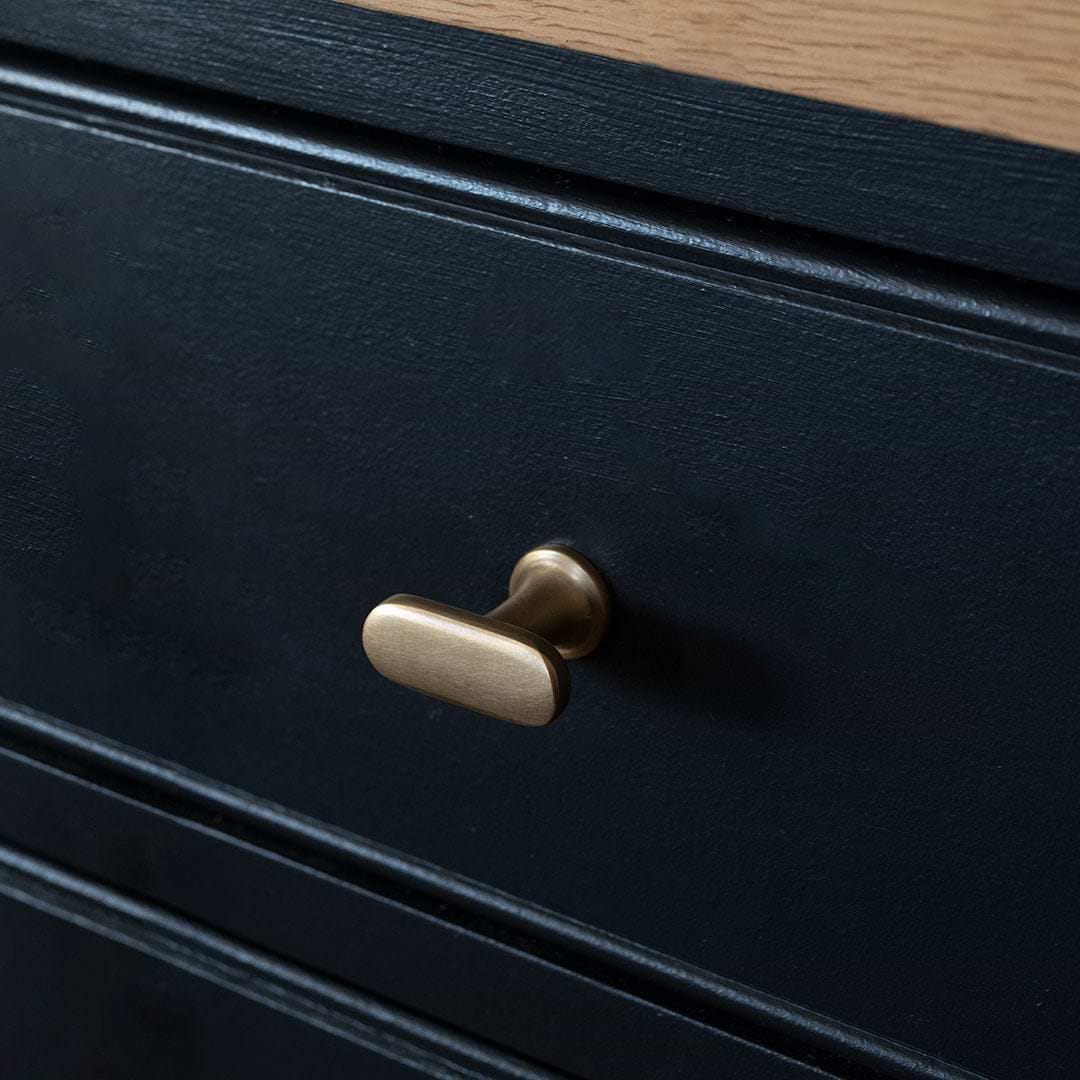 Close-up of a Milliner Furniture Knob in antique brass finish installed on a dark drawer front.