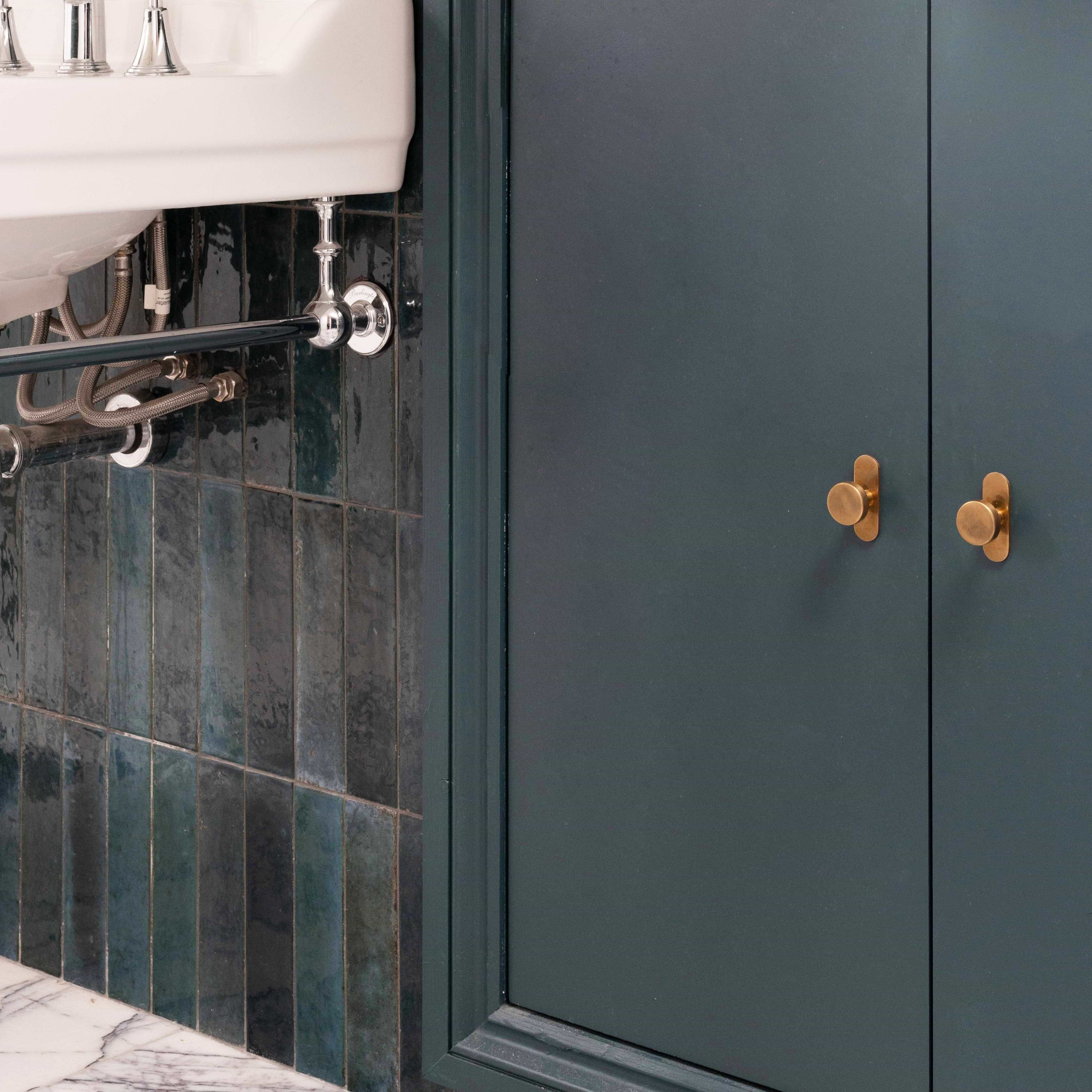 Polished Kilburn Furniture Knobs in gold finish on a matte green cabinet above a white marble floor.