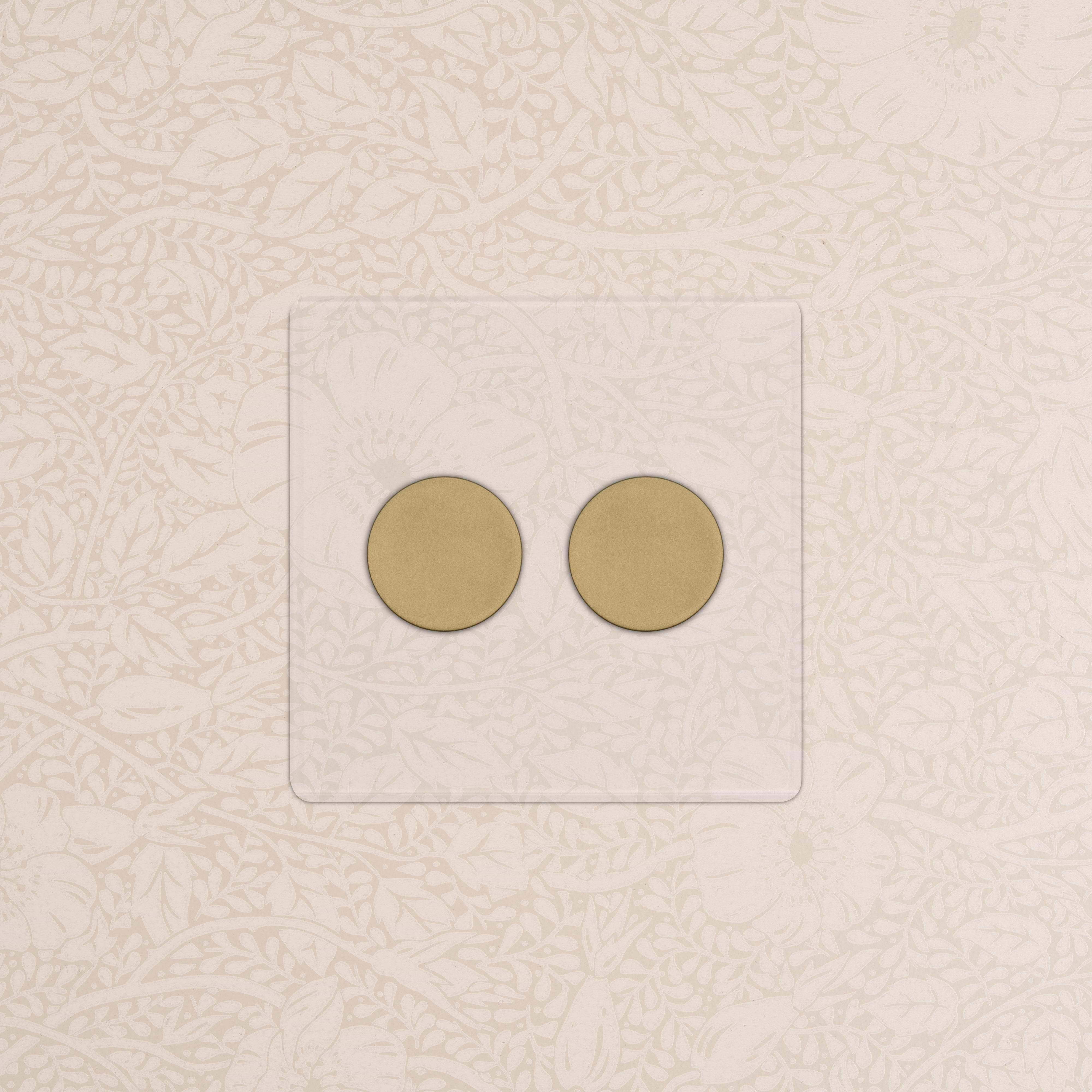 Kew 2G Dimmer Switch in Clear Antique Brass with two round dimmer knobs on a decorative wall.