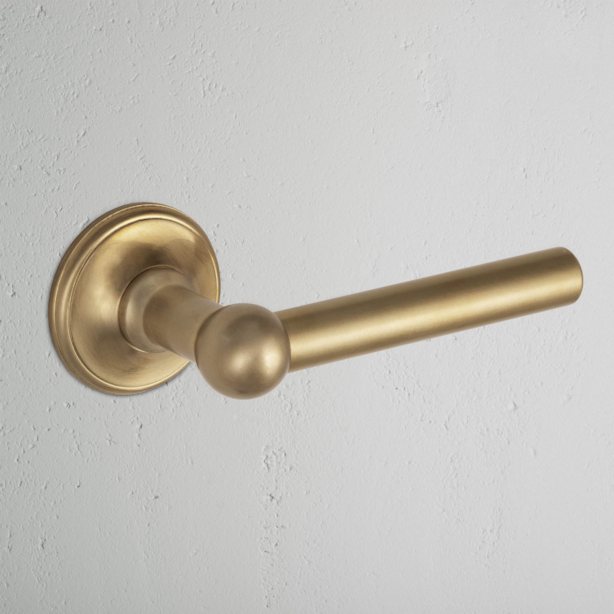 Harper Passage Door Handle Set in antique brass with a round baseplate, mounted on a white wall.