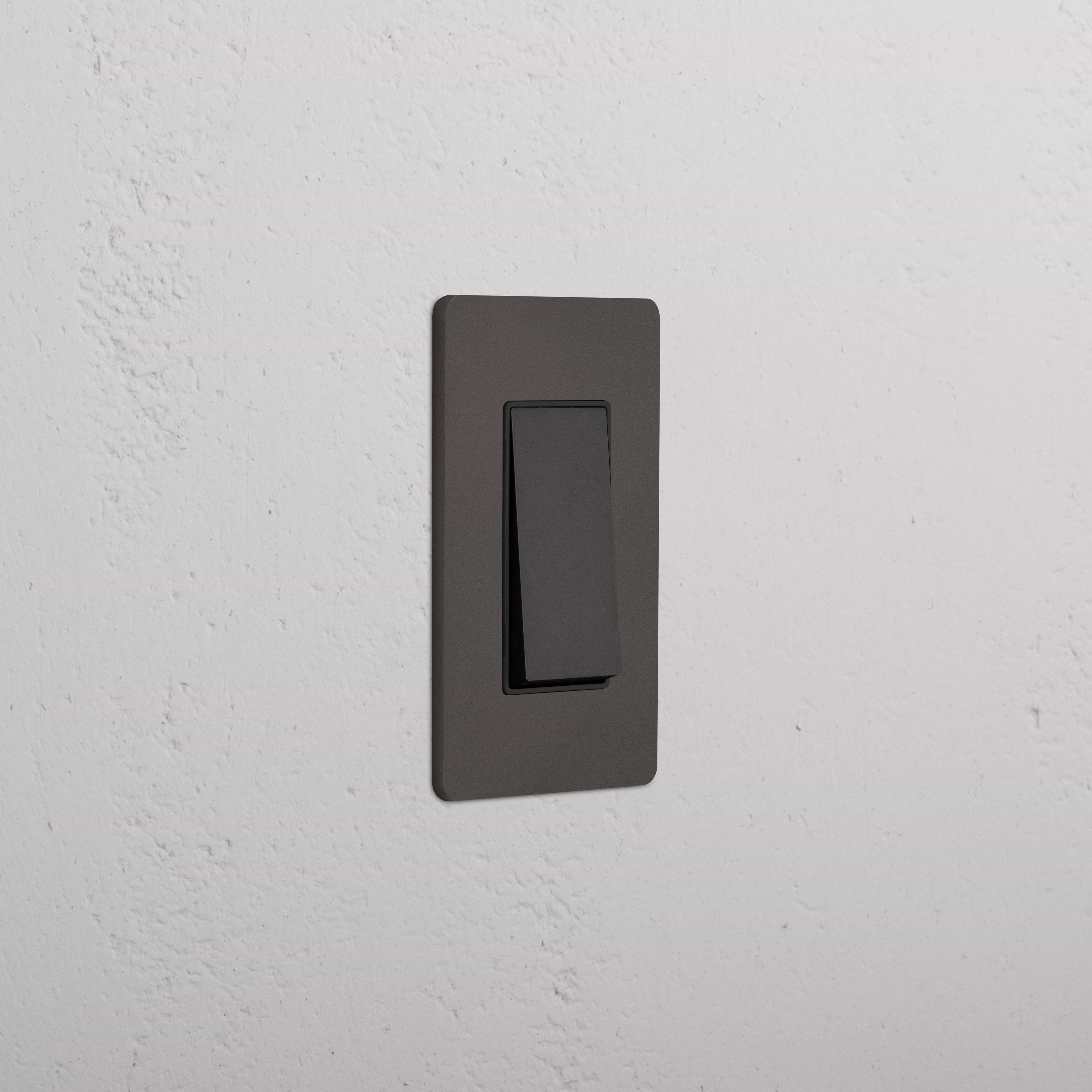 Grove 1G Retractive Rocker Switch in Bronze Black, single rectangular switch on a white textured wall.