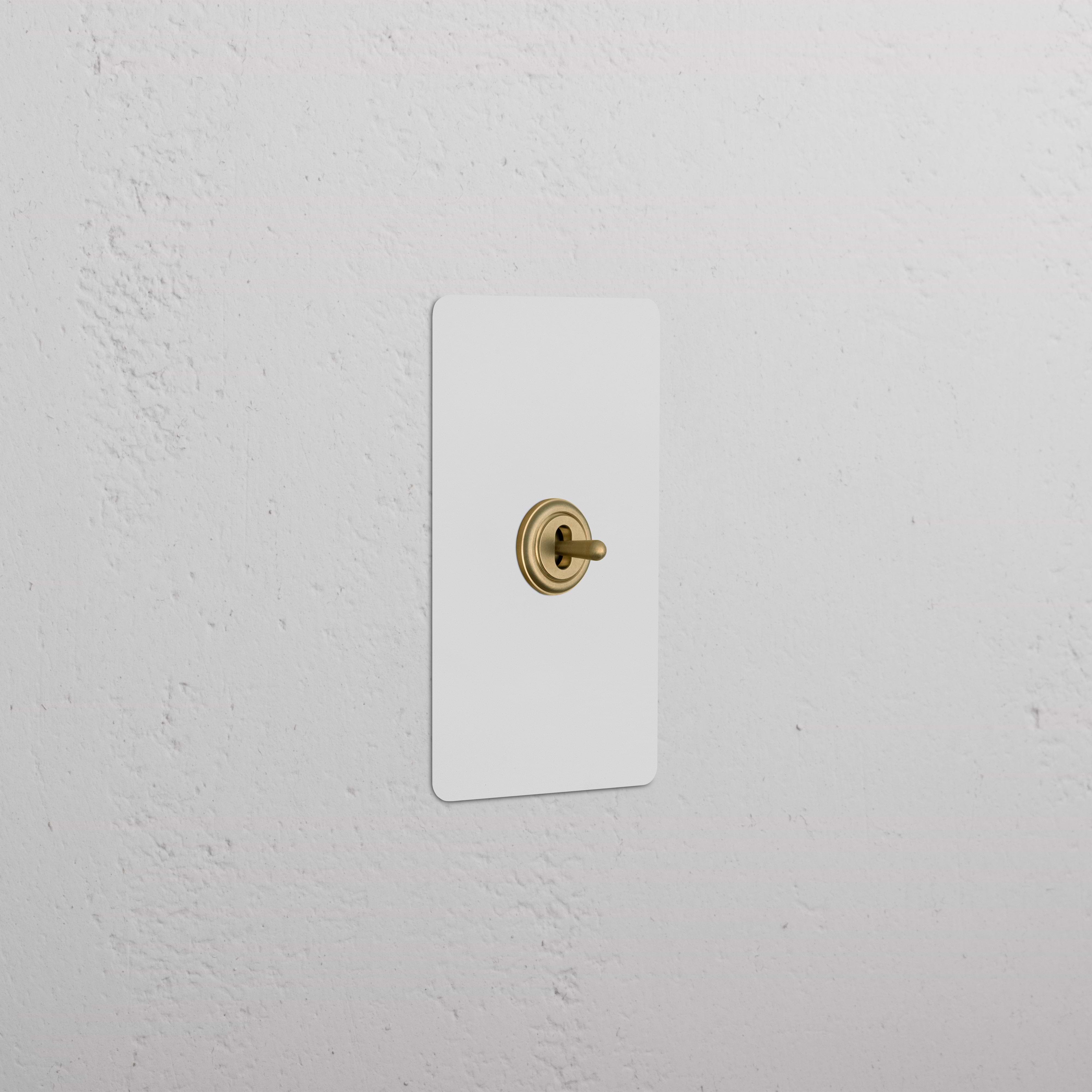 Kew 1G Center Retractive Toggle Switch in paintable antique brass with white plate, mounted on a white wall.