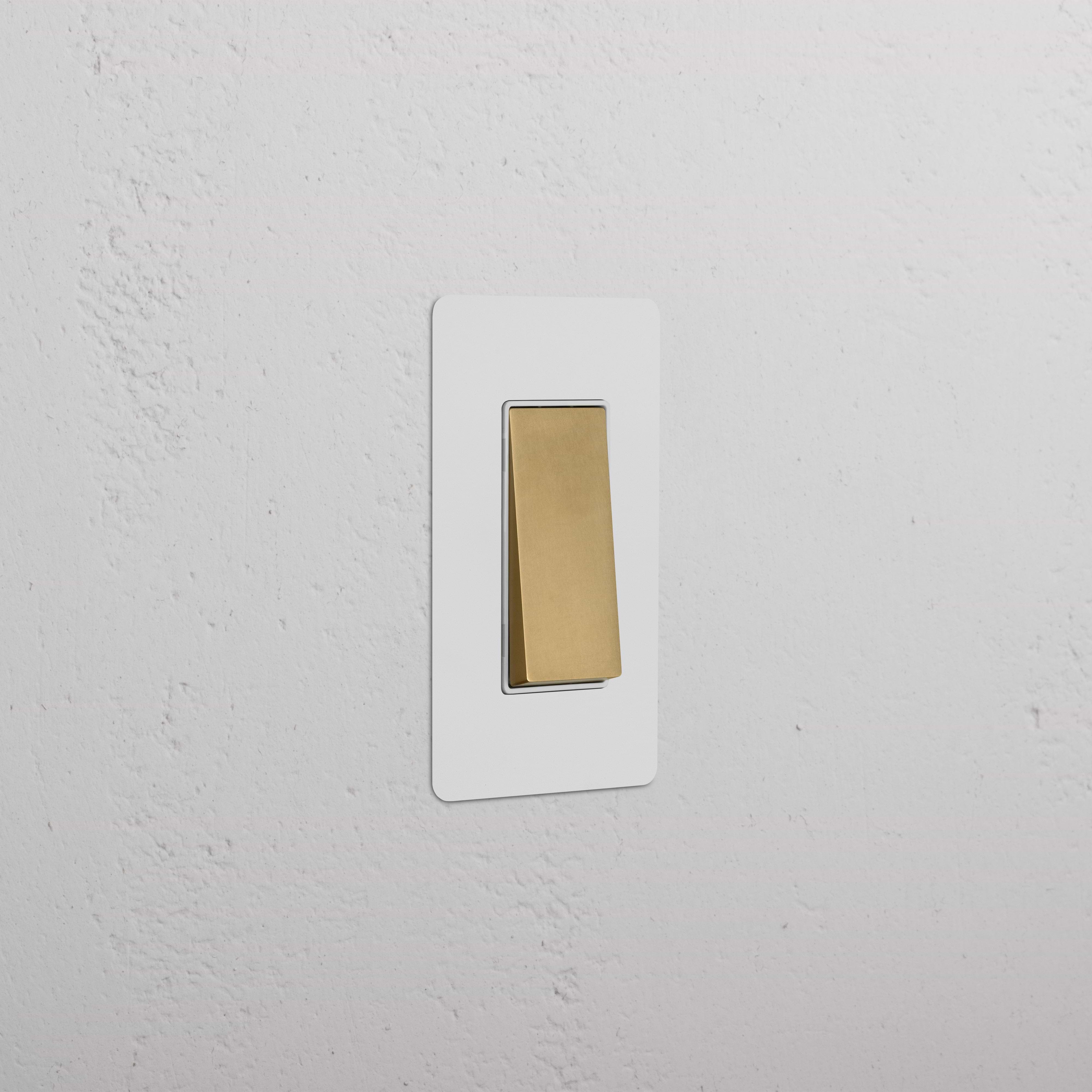 Kew 1G Retractive Rocker Switch in paintable antique brass with white faceplate, mounted on a white wall.