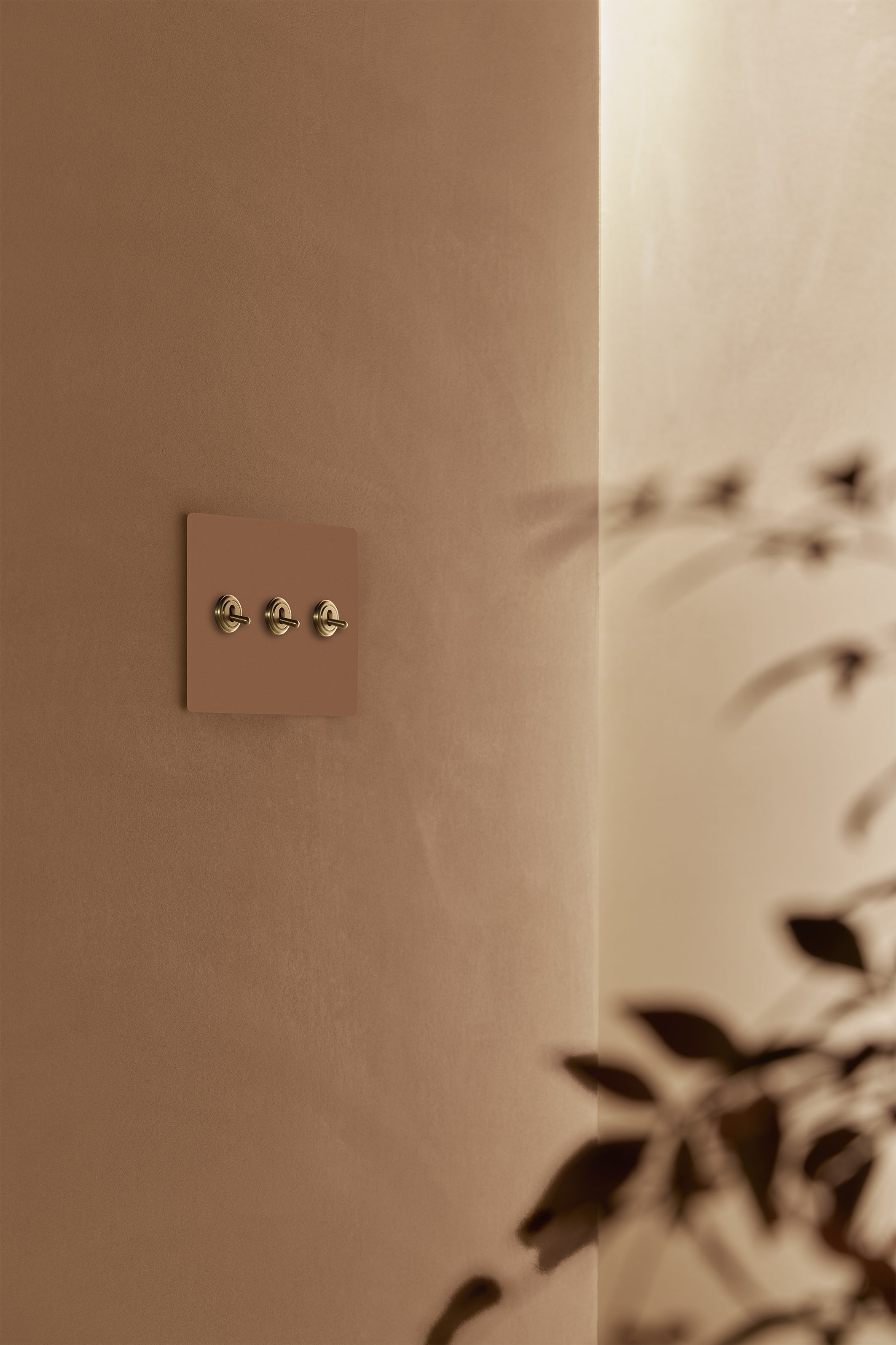 Kew 3G Toggle Switch in Paintable Antique Brass mounted on a wall, suitable for customizable finishes.