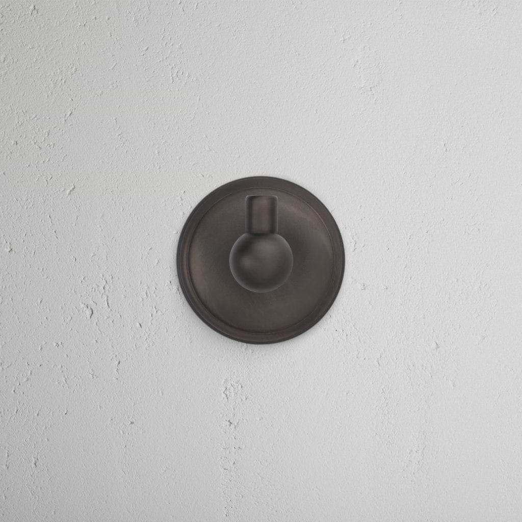 Hyde Hook - Bronze: a modern, round bronze wall hook with a circular base and short peg, mounted on white wall.