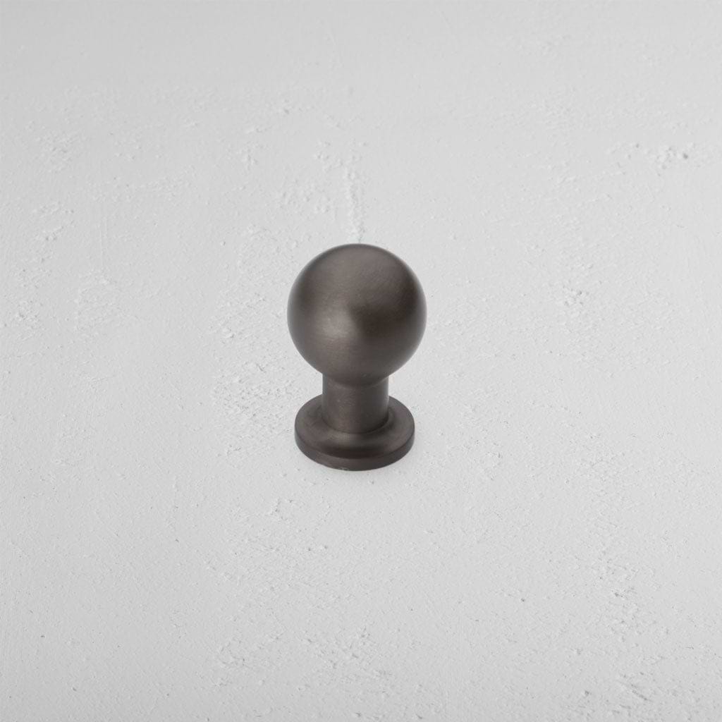 Small round bronze Bayswater Furniture Knob with a short cylindrical base on a white textured surface.
