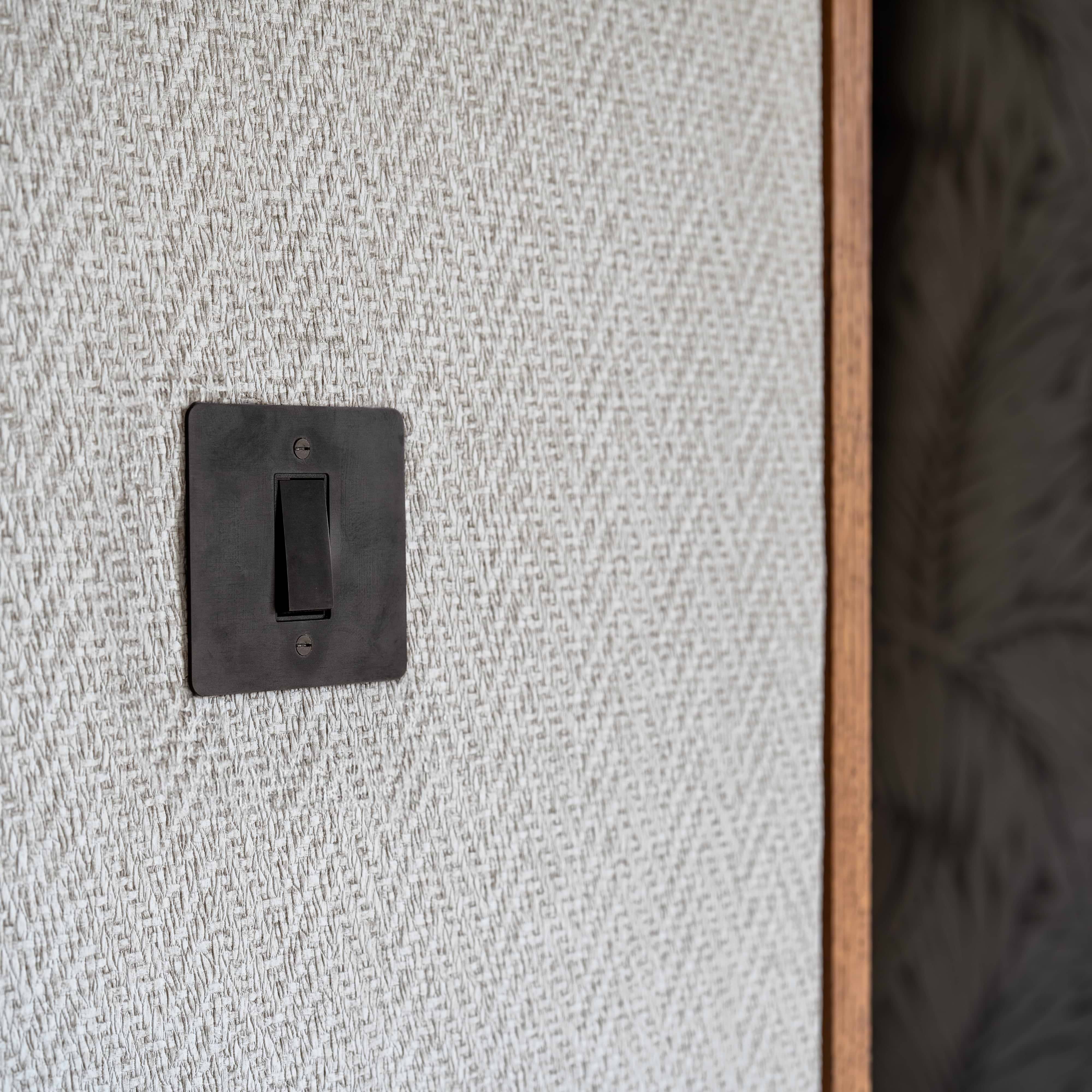 Kew 4G Rocker Switch in Bronze Black finish installed on a wall, with wooden door frame to the right.