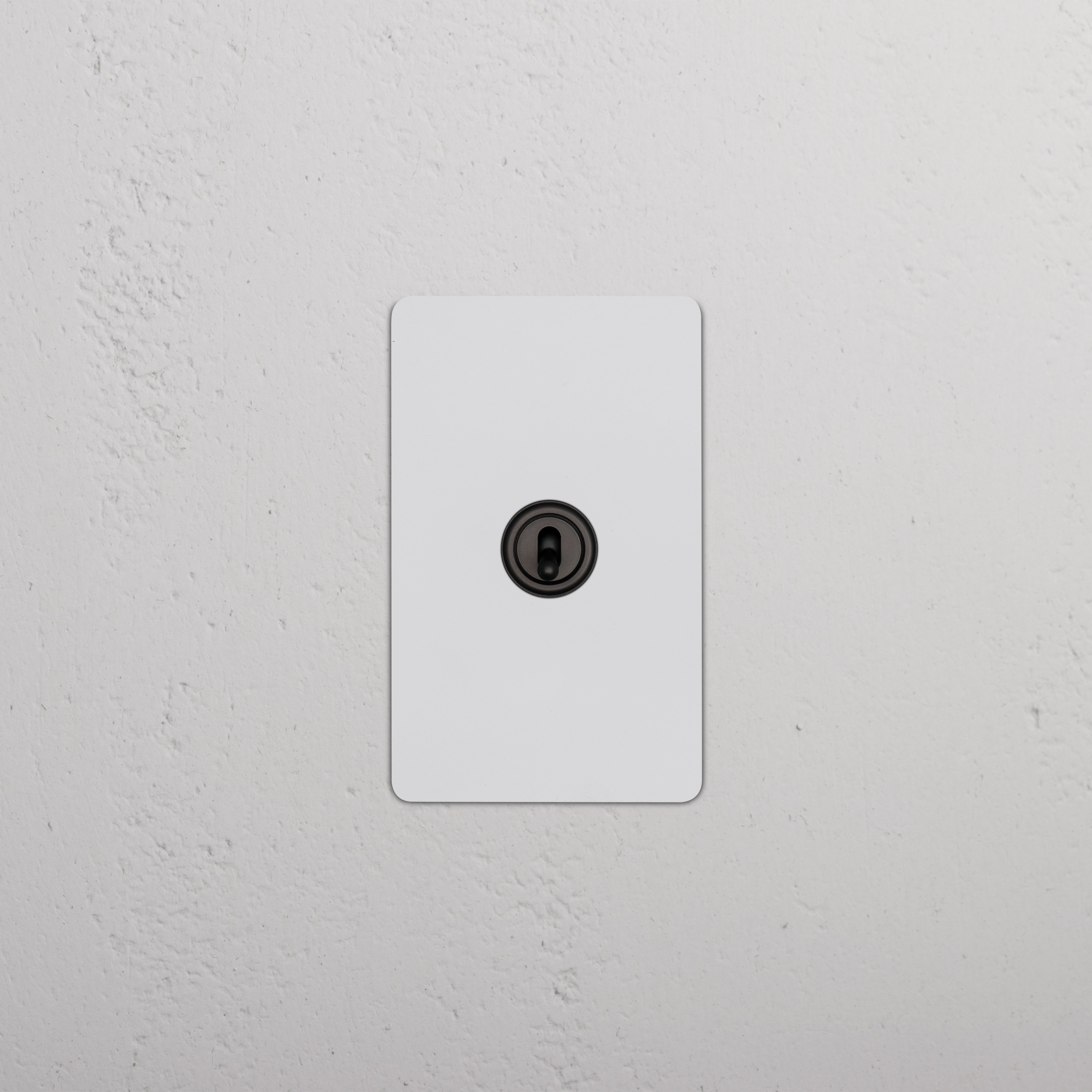 Kew 1G Retractive Toggle Switch in paintable bronze finish, shown mounted on a wall.