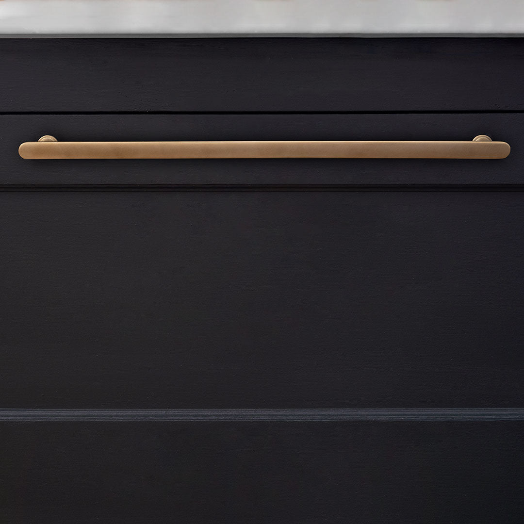 Large Milliner Furniture Handle in antique brass mounted on a cabinet beneath a white countertop.