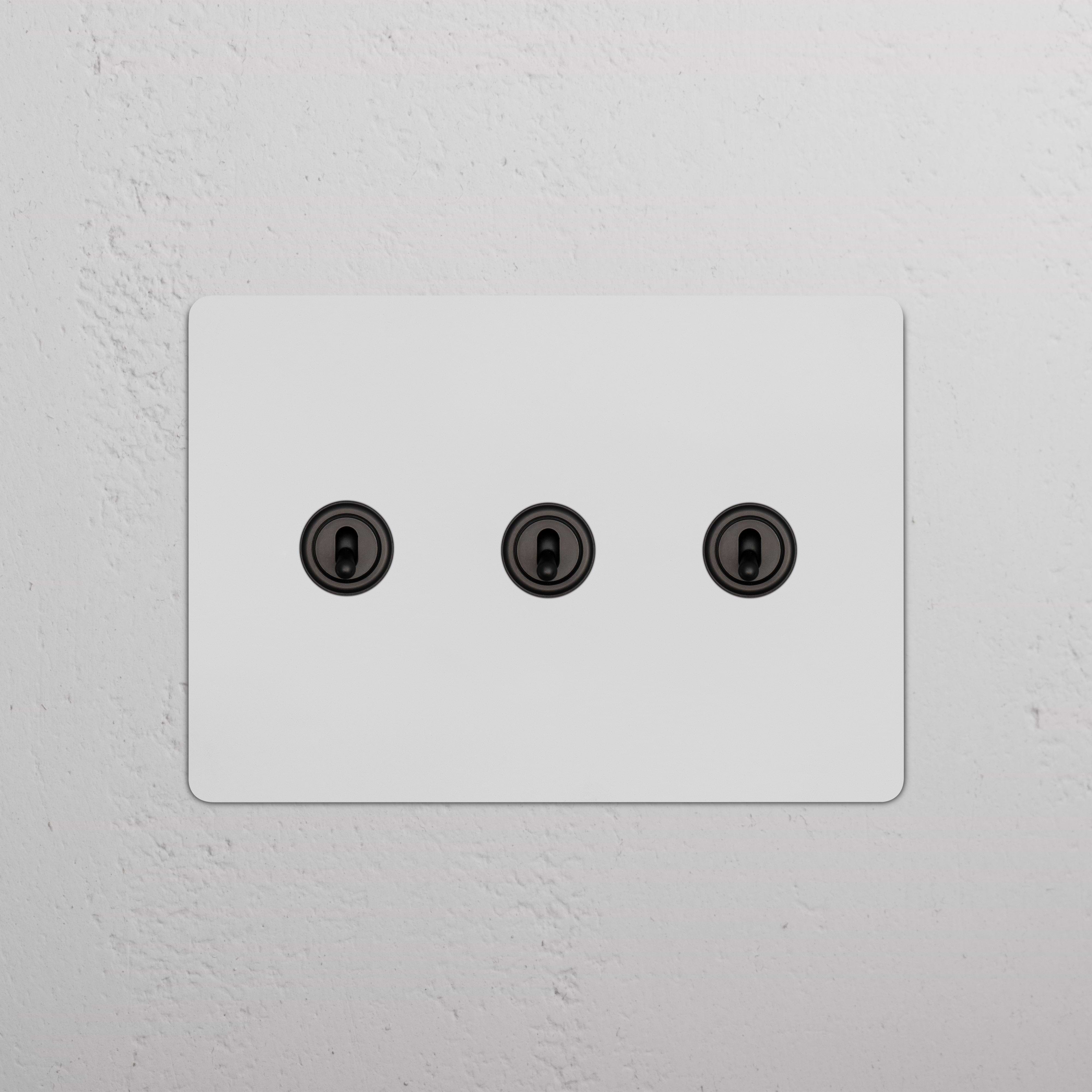 Kew 3G Toggle Switch in paintable bronze finish with three horizontal black toggles, suitable for wall mounting.