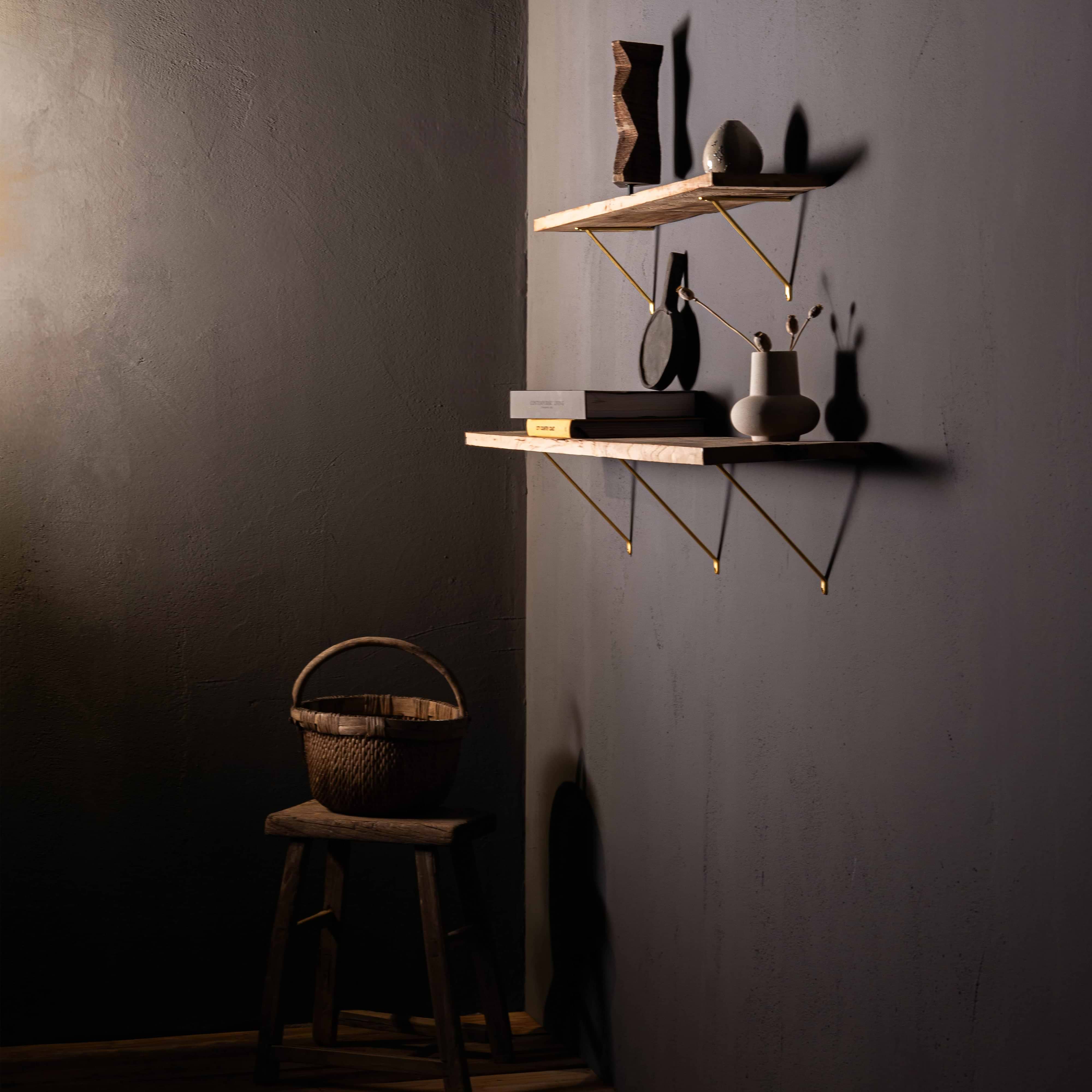 Brixton Shelf Bracket Medium in antique brass supports wooden shelves mounted on a gray wall.