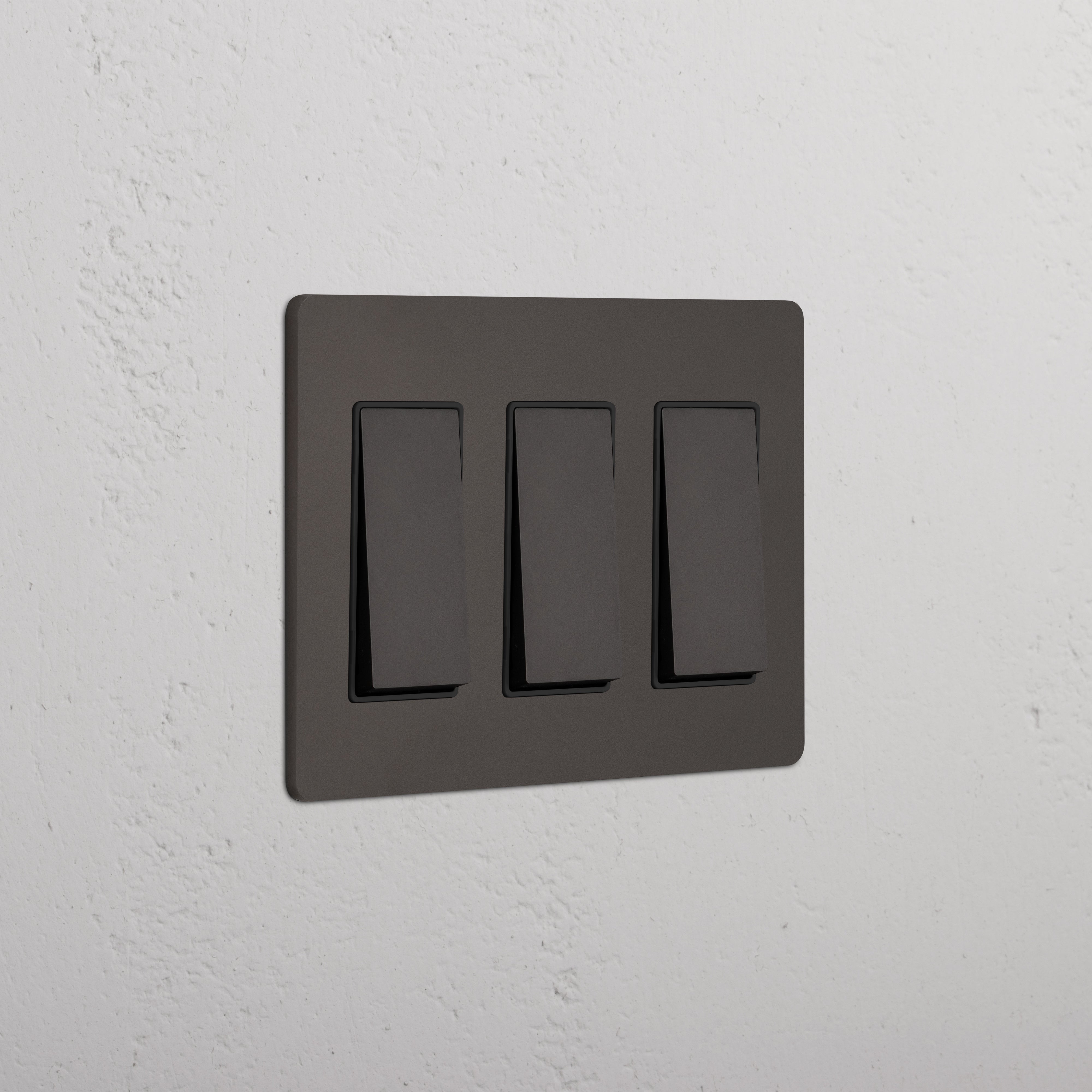 Grove 3G Rocker Switch in Bronze Black, triple light switch panel mounted on a textured white wall.