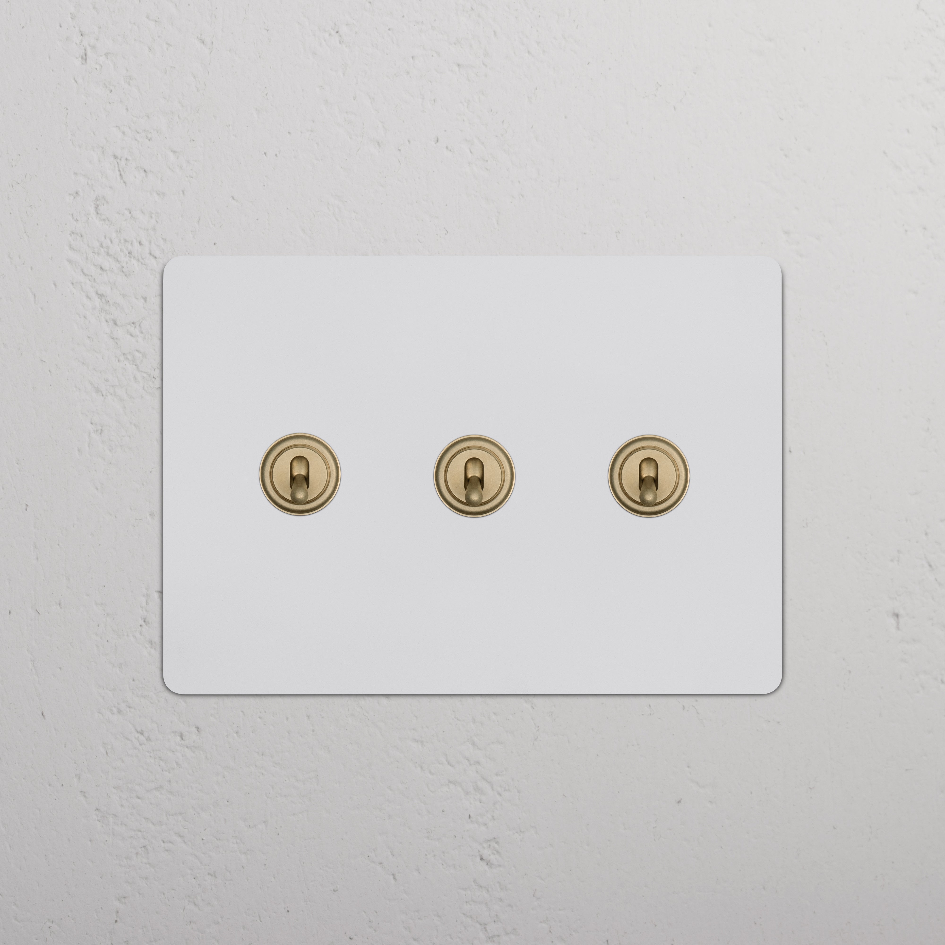 Kew 3G Toggle Switch in paintable antique brass with three horizontal gold toggles on a wall plate.