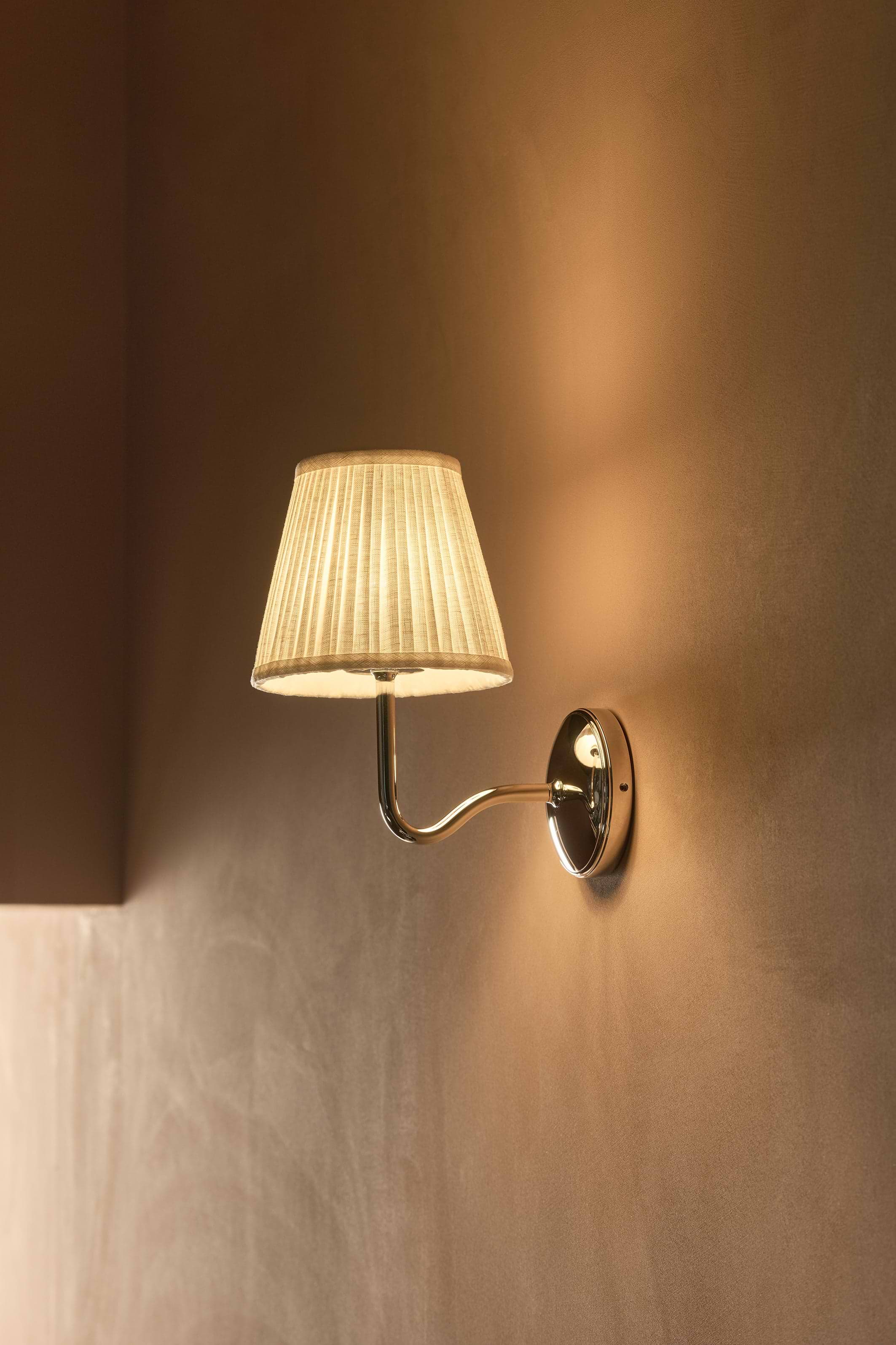 Malvern Medium Wall Light Alabaster White with pleated shade and polished nickel arm, illuminated on a plain wall.