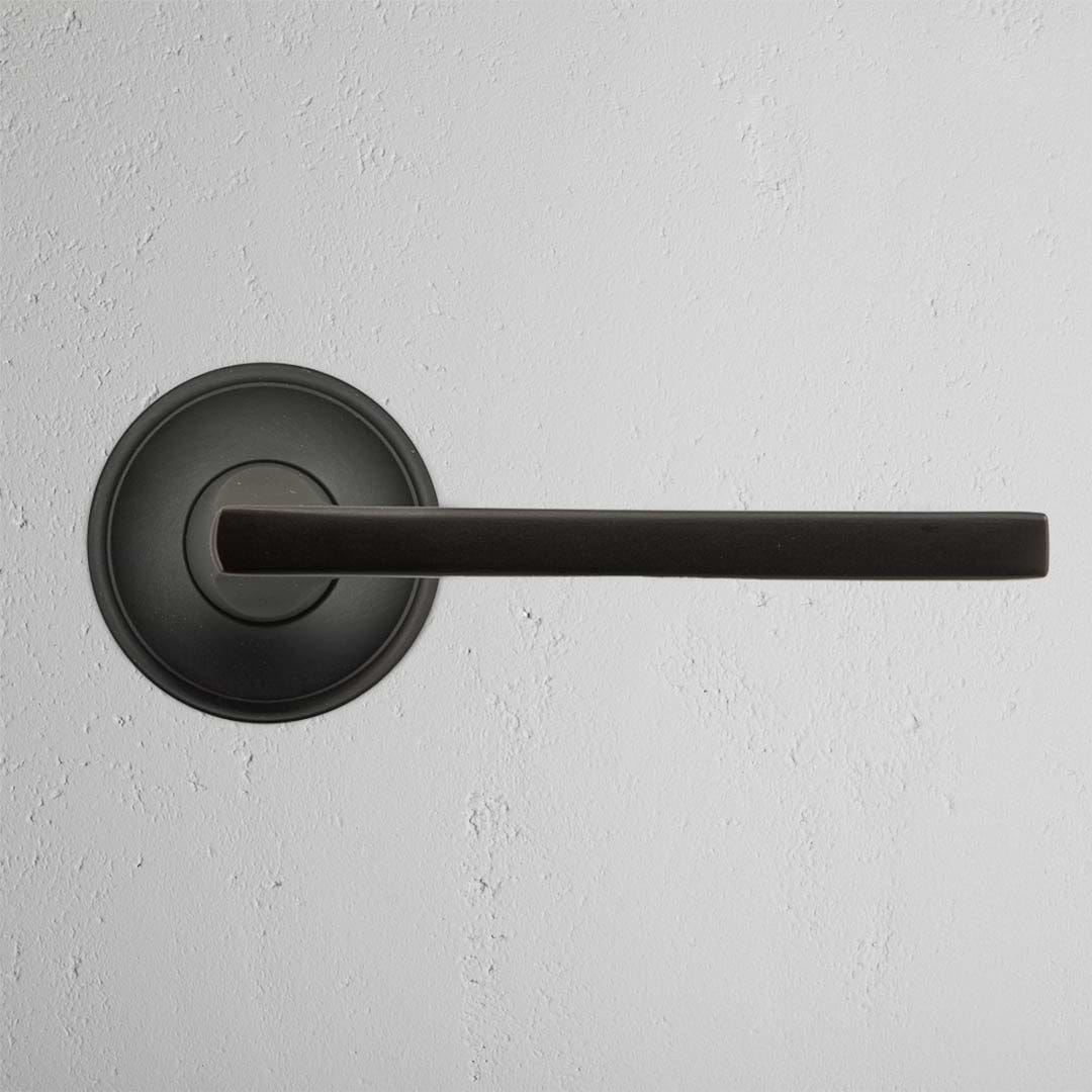Clayton Unsprung Passage Door Handle Set in bronze with round base, shown mounted on a light-colored wall.
