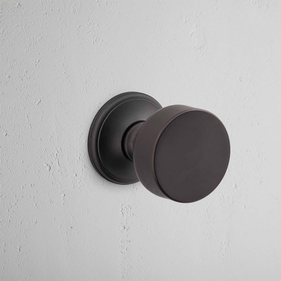 Bronze Onslow Passage Door Knob Set with a simple, modern design mounted on a light textured white wall.