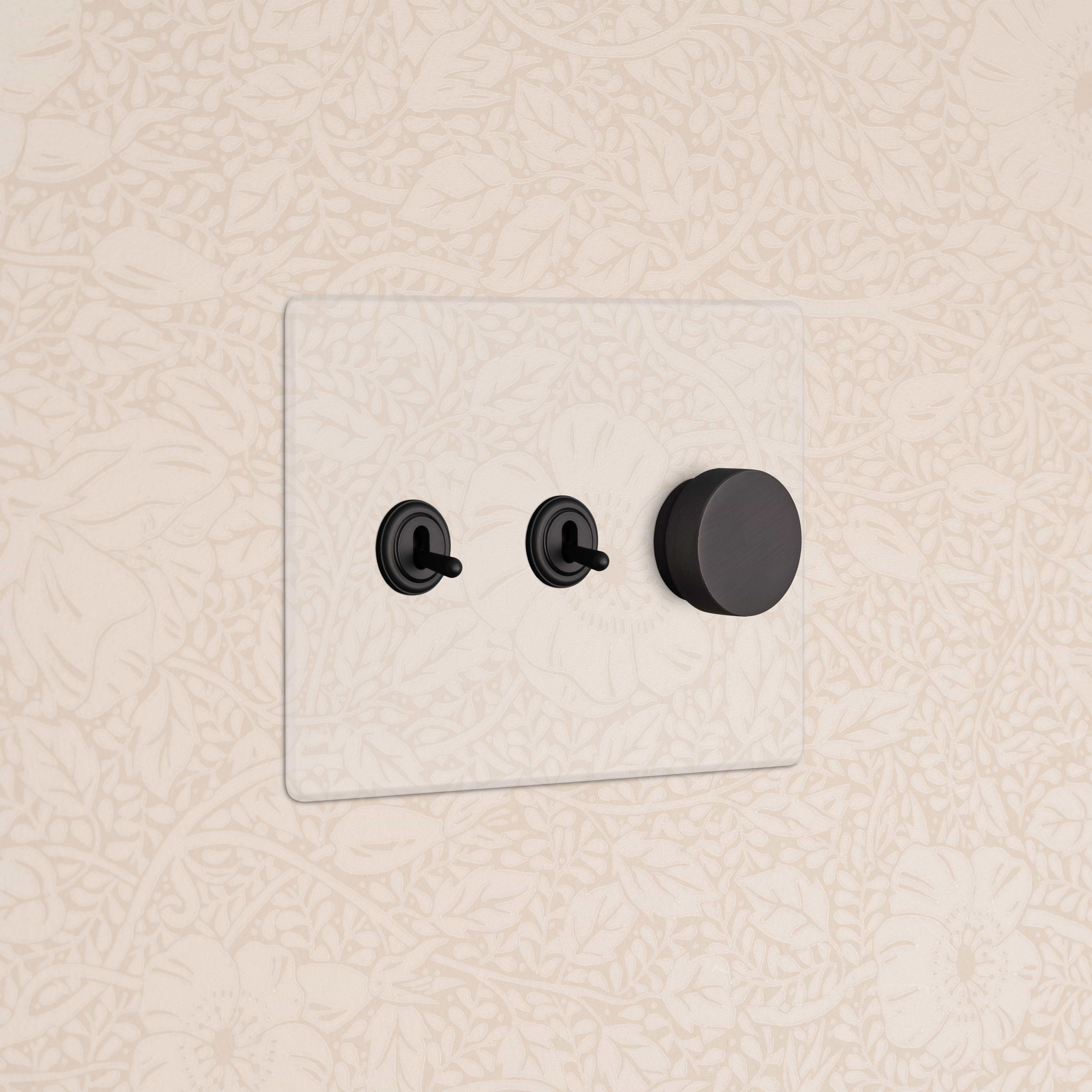 Kew 3G 2x Toggle & Dimmer Switch in Clear Bronze with two toggles and one rotary dimmer on a wall.