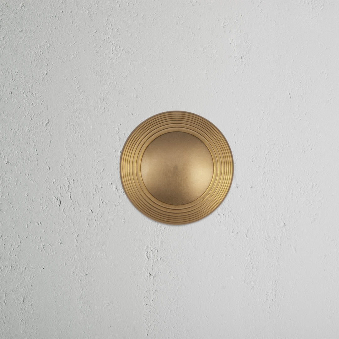 Poplar Passage Door Knob Set in antique brass finish, featuring concentric ring details, on a white wall.