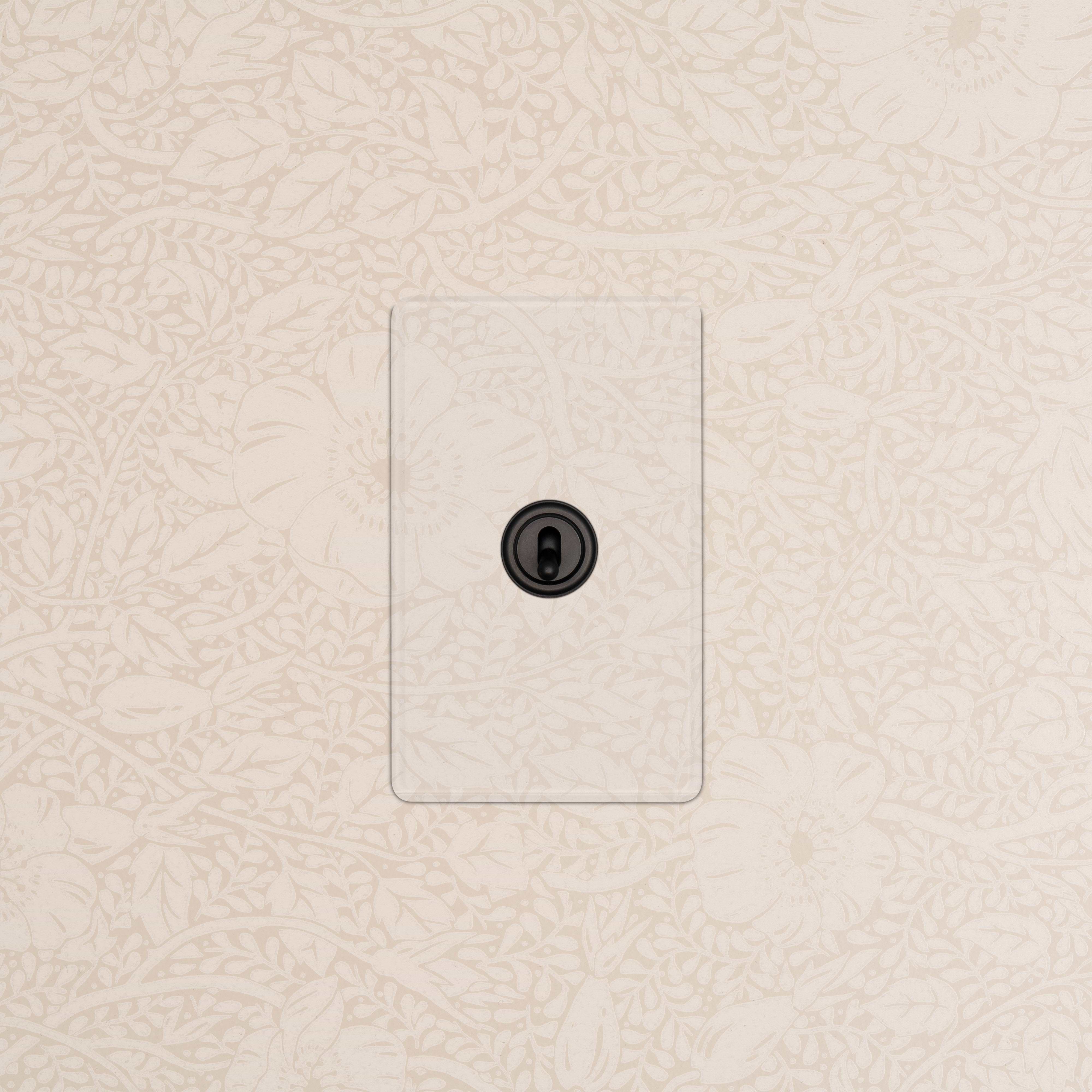 Kew 1G Four Way Toggle Switch in clear bronze finish, mounted on a wall with a light floral pattern.