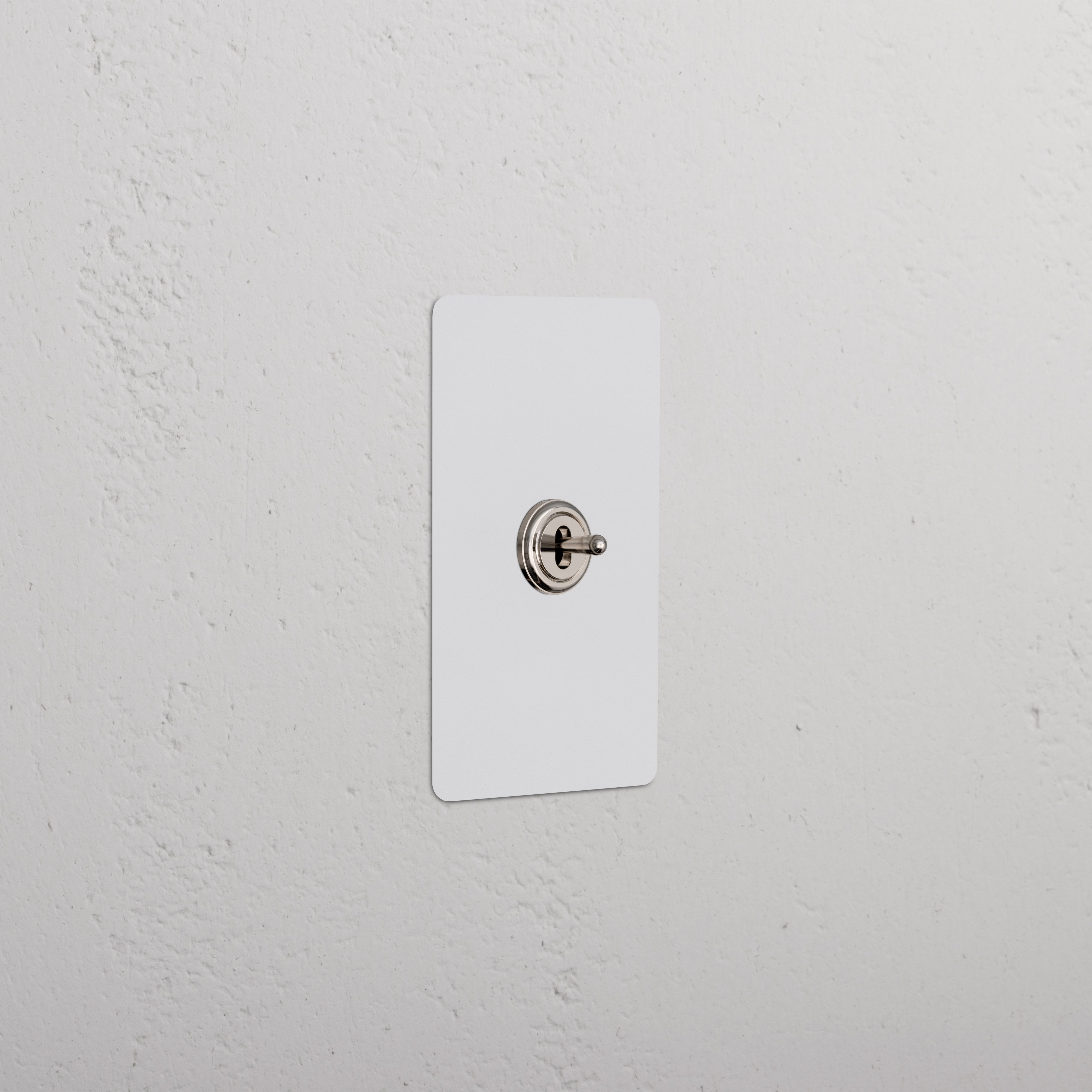 Kew 1G Center Retractive Toggle Switch in paintable polished nickel, mounted on a white textured wall.