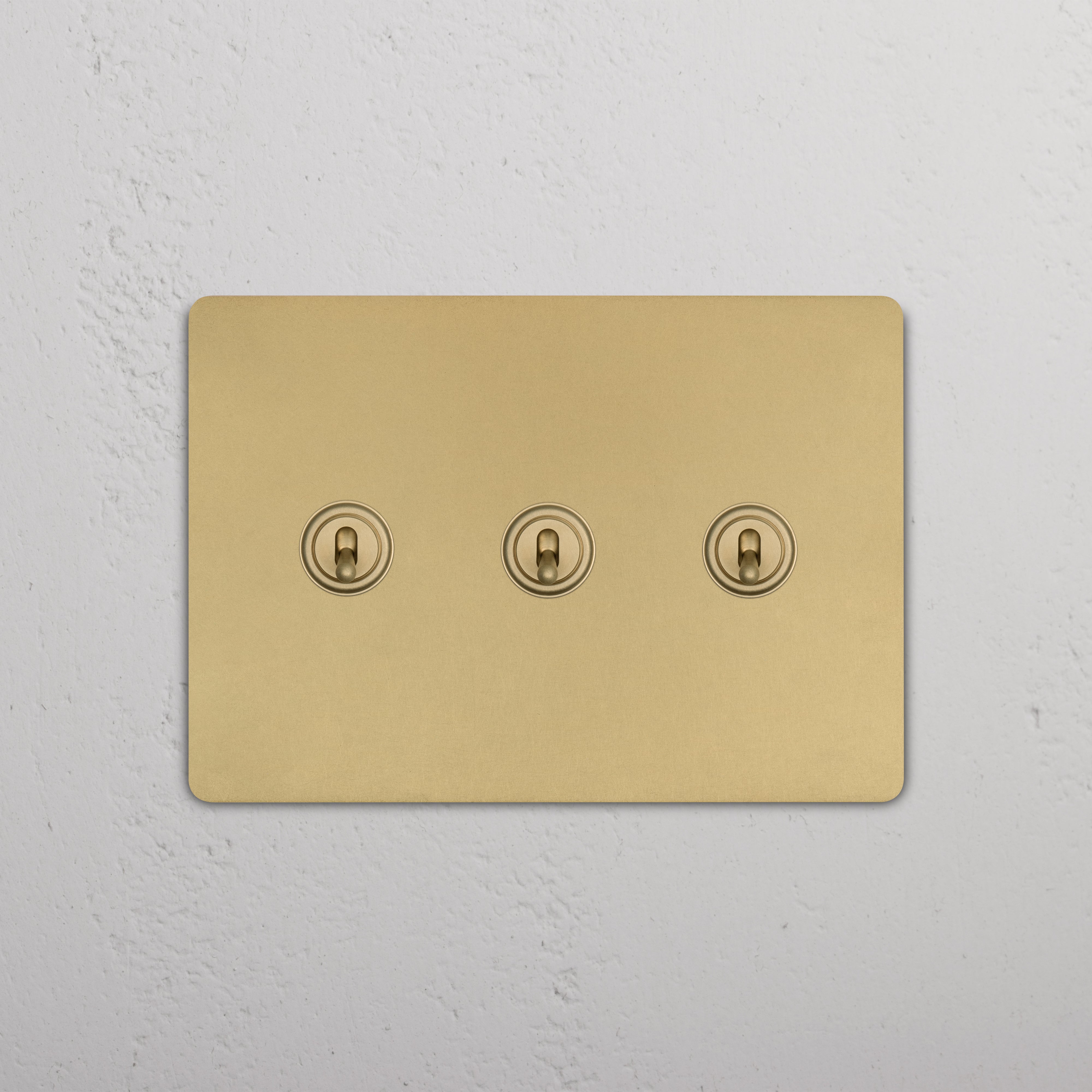 Grove 3G Toggle Switch in antique brass finish with three toggles, shown on a white textured wall.