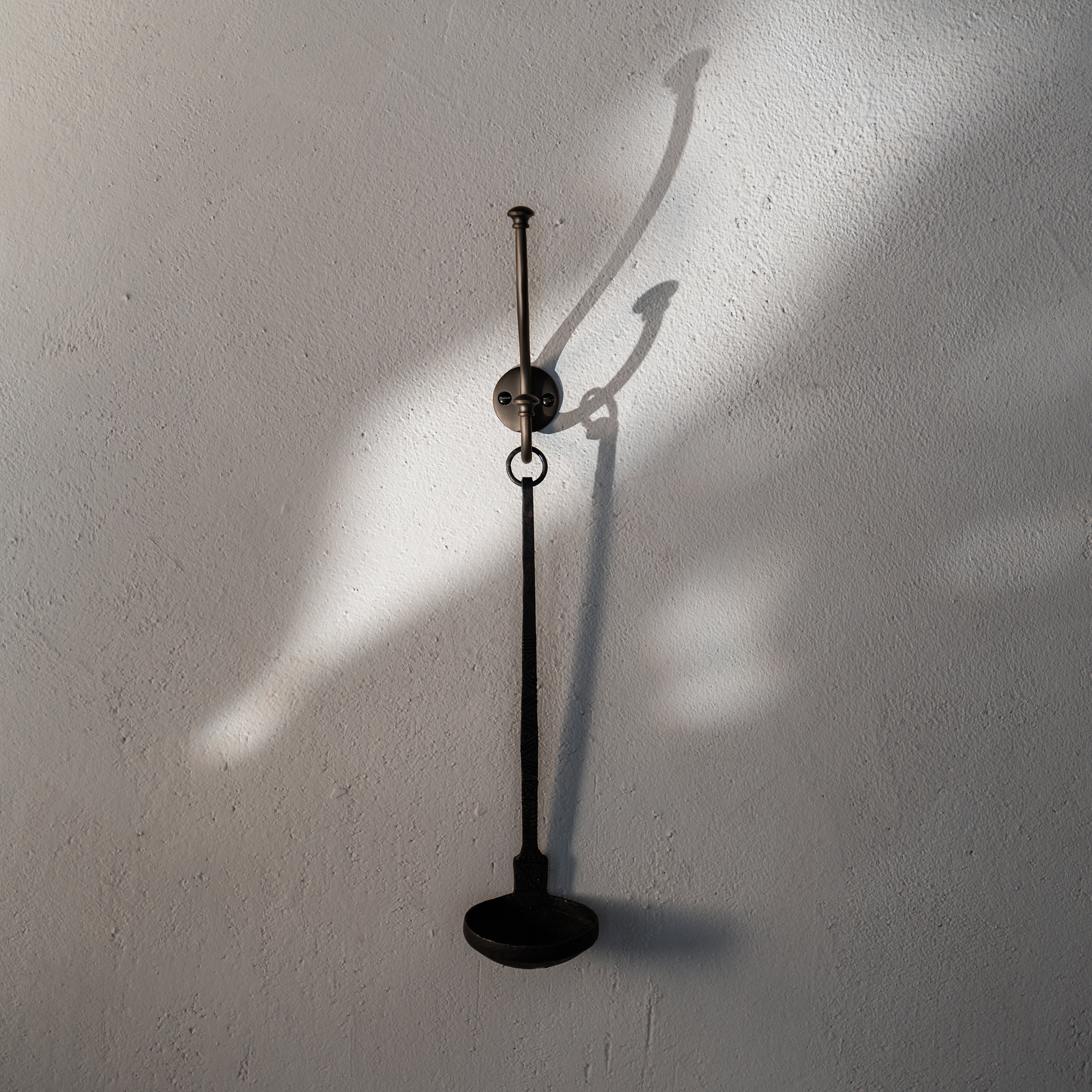 Bronze Mews Hook mounted on a white textured wall, displaying its sleek, functional design.