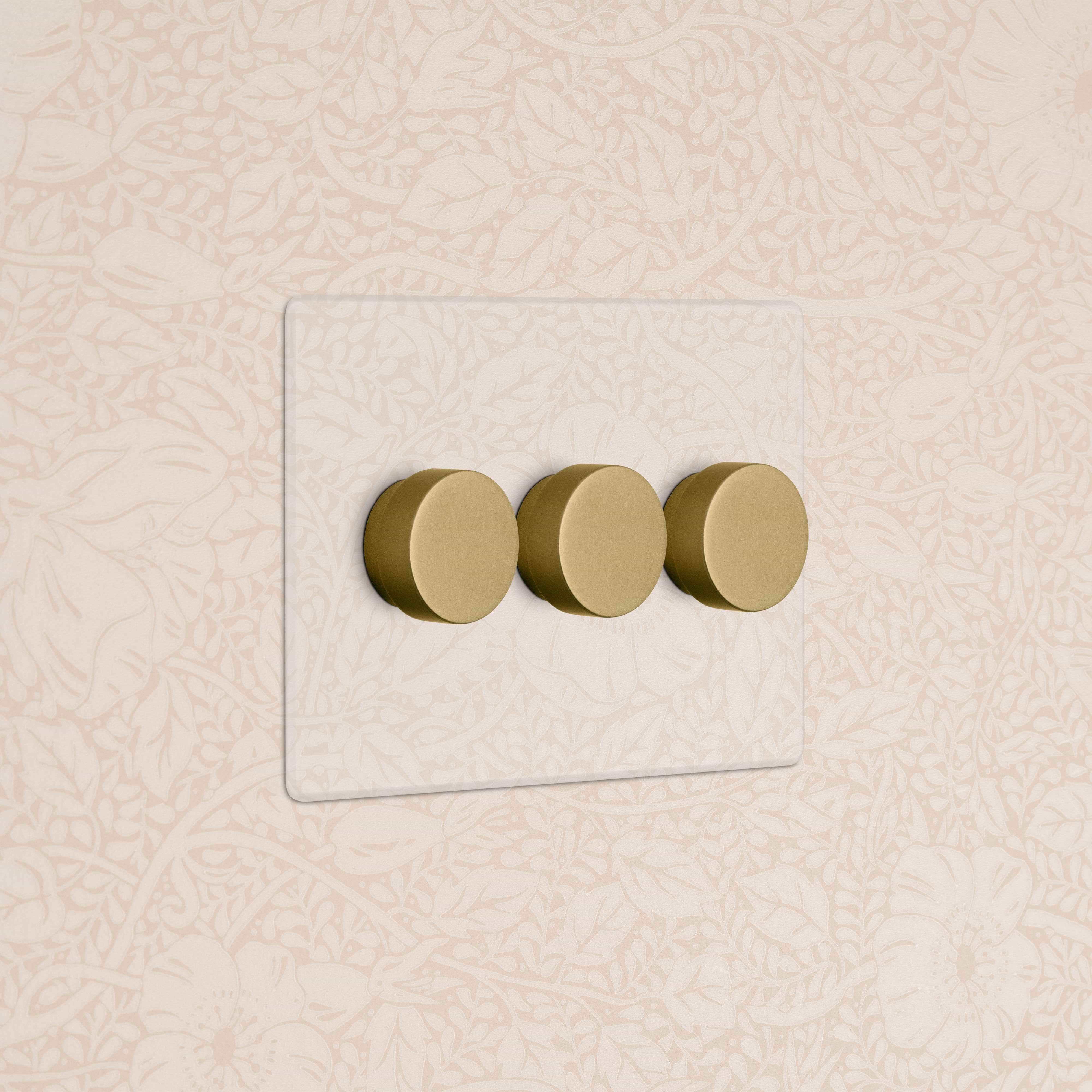 Kew 3G Dimmer Switch in Clear Antique Brass with three round brass dimmer knobs on a glass plate.