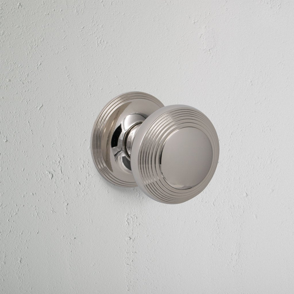 Polished nickel Poplar Dummy Door Knob Set with round, ridged design mounted on a white wall.