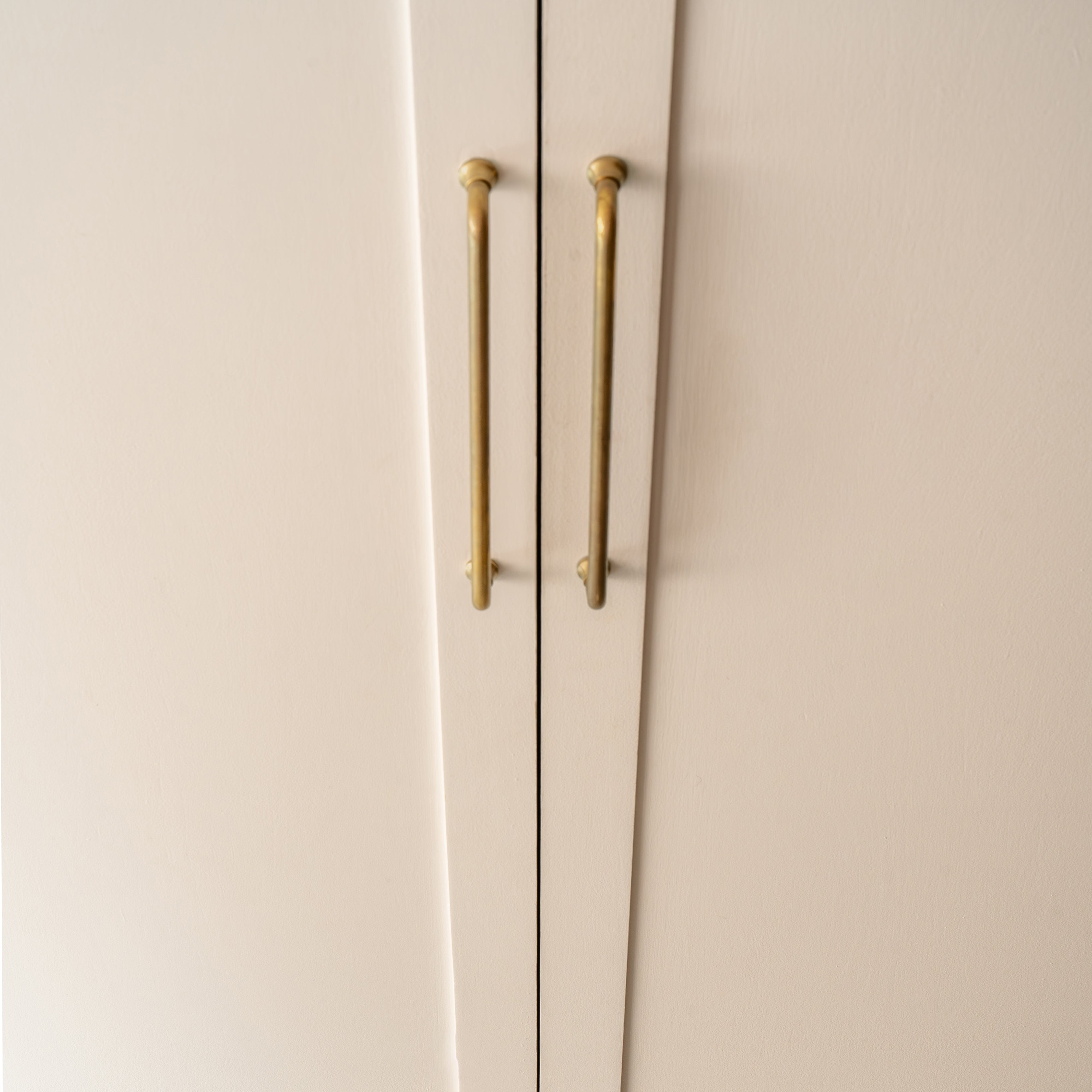 Pair of Sycamore Furniture Handle Large in antique brass, vertically mounted on light cabinet doors.