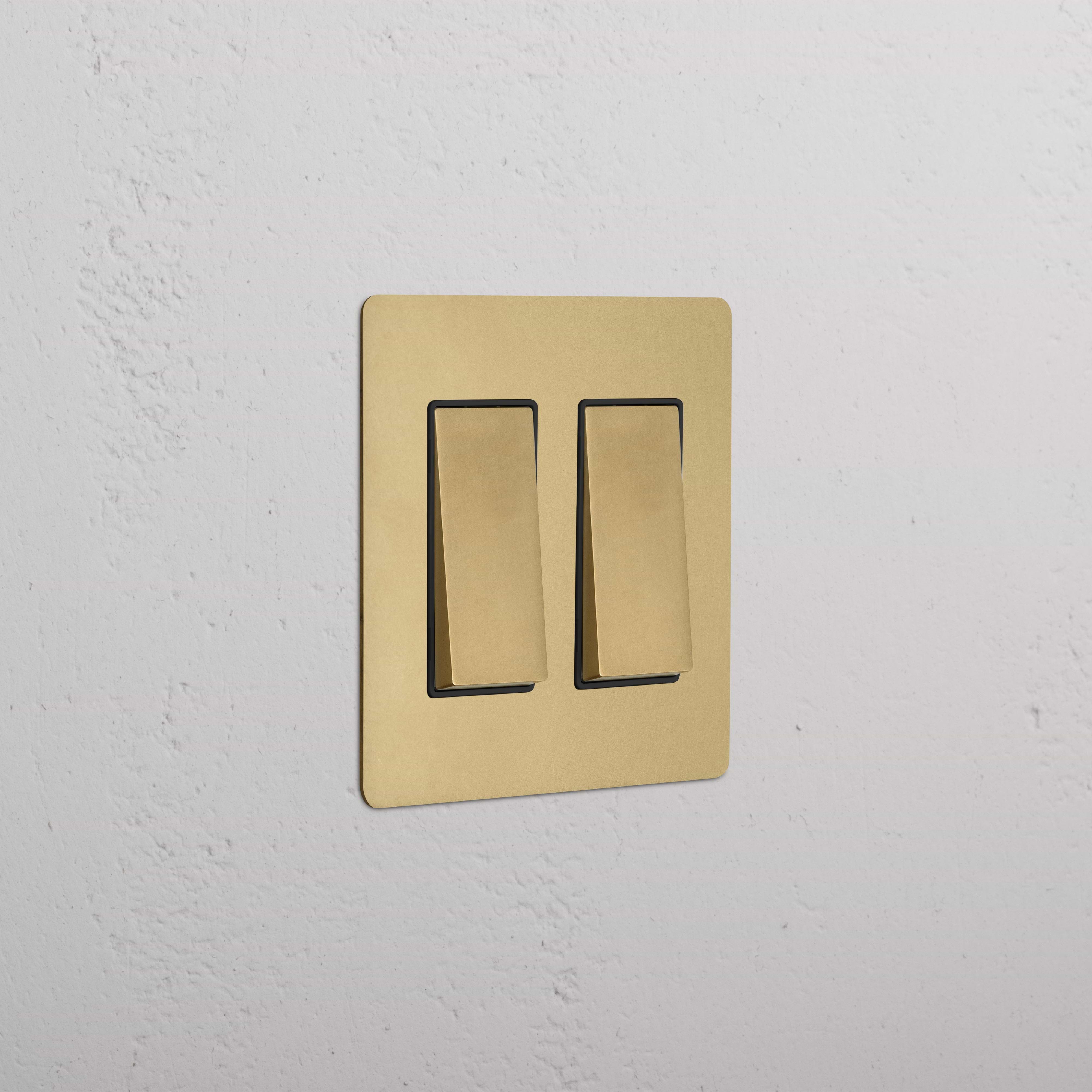 Kew 2G Rocker Switch in antique brass with black inserts, mounted on a white textured wall.