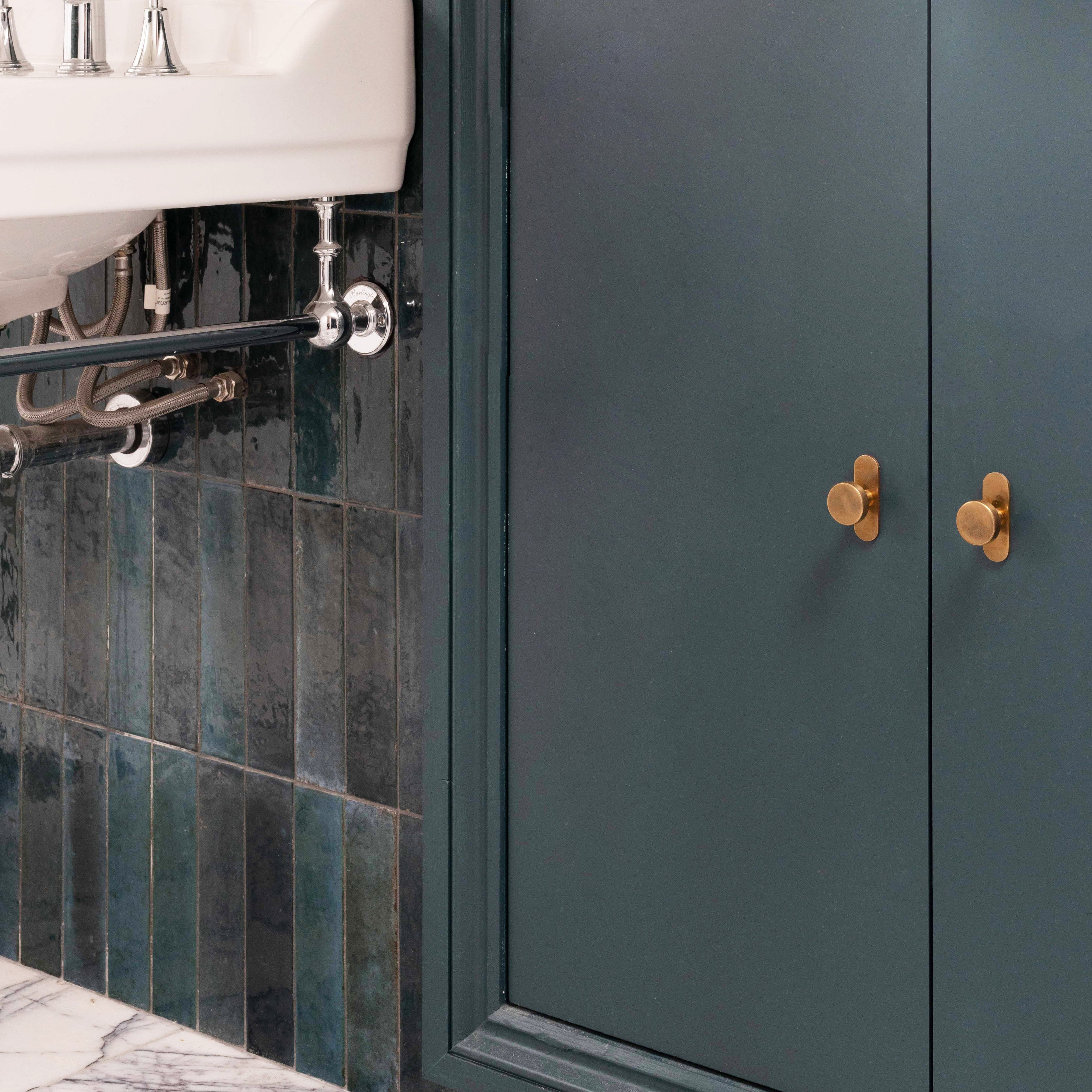 Polished Kilburn Furniture Knobs in gold finish on a matte green cabinet above a white marble floor.