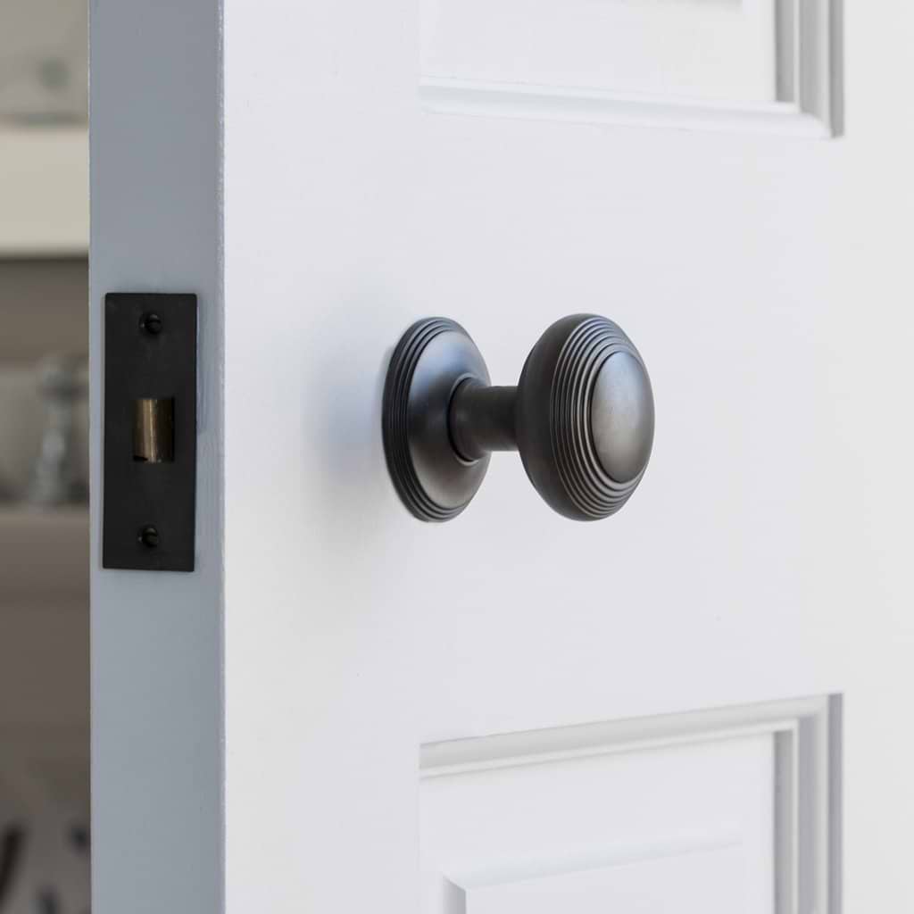 Close-up of a bronze Poplar Dummy Door Knob Set installed on a white door.