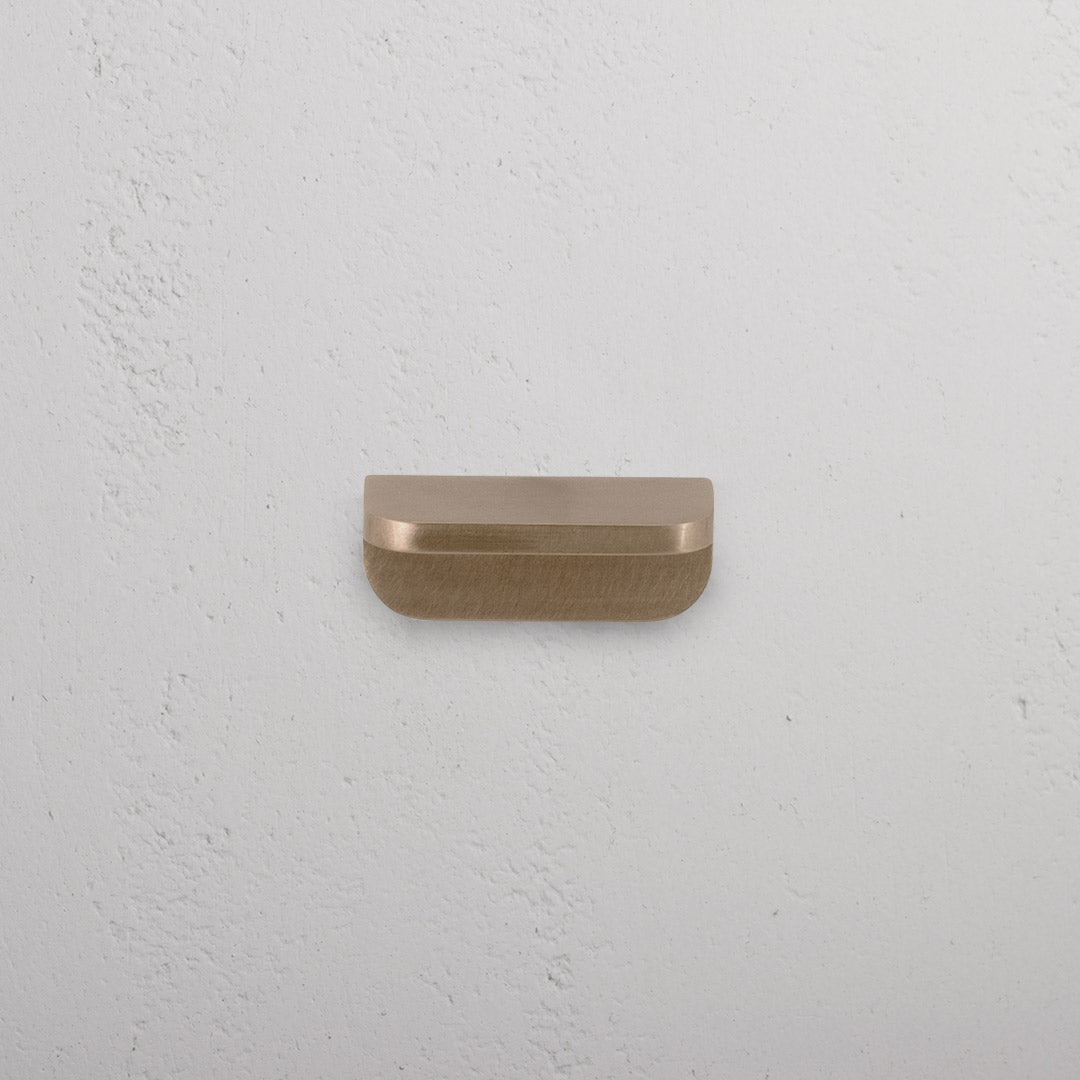 An extra small Oxford furniture handle in antique brass finish, mounted on a white surface.