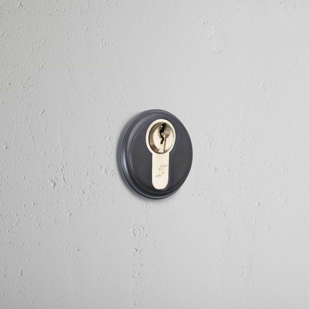 Bronze Canning Key Escutcheon with a circular design, mounted on a light gray textured wall.