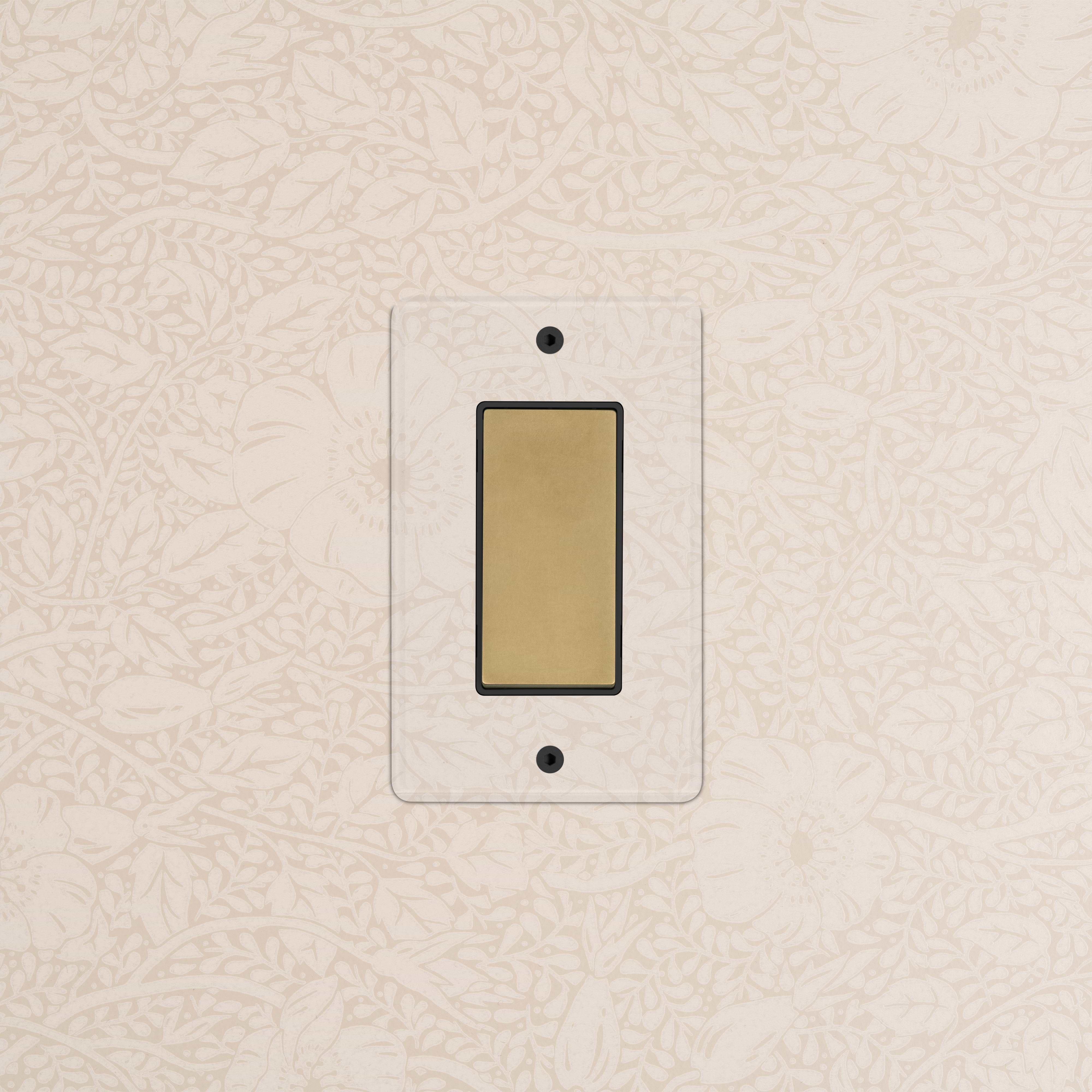 Kew 1G Dimming Retractive Rocker Switch in clear antique brass black, mounted on a floral wallpapered wall.
